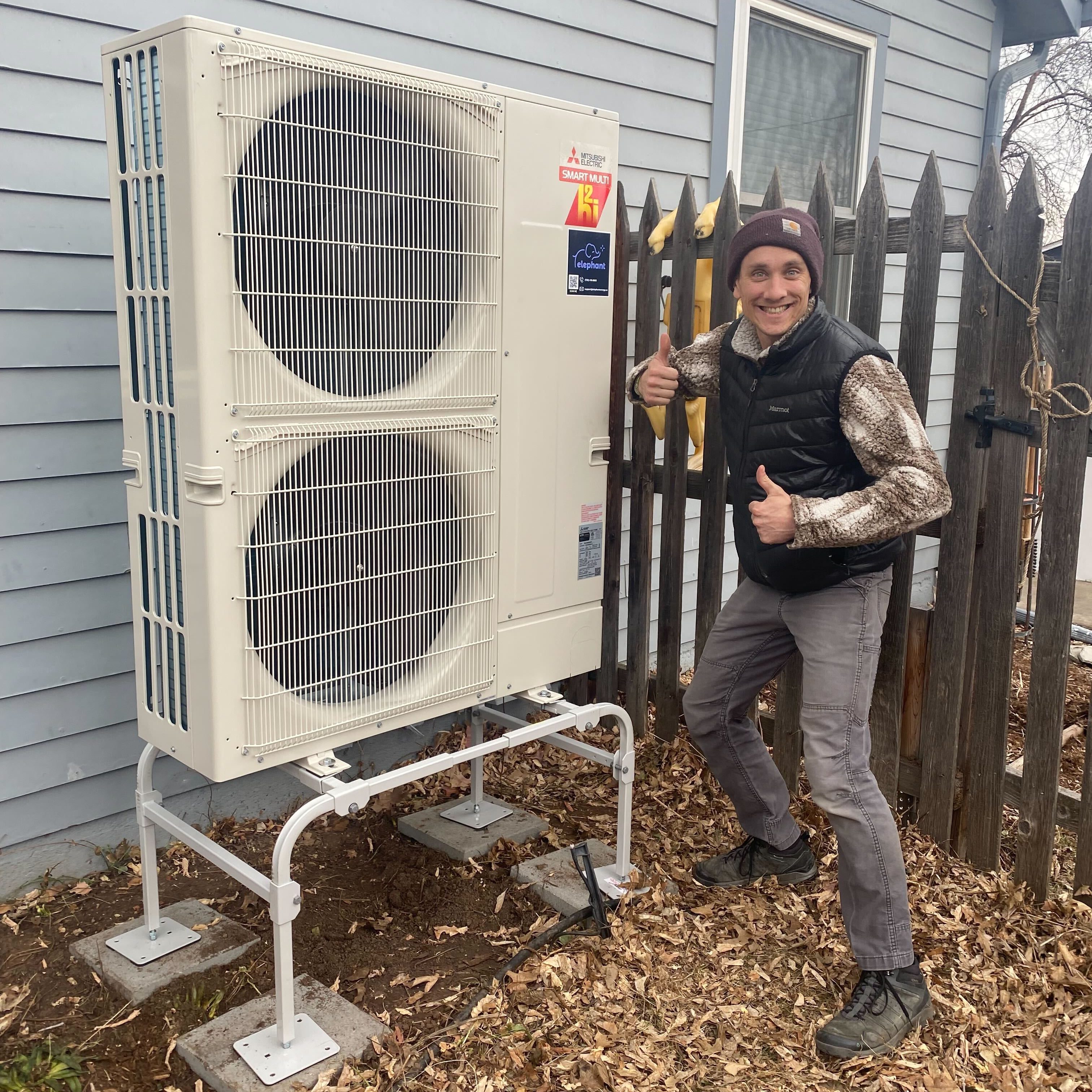 Elephant Energy team member smiling in front of a heat pump