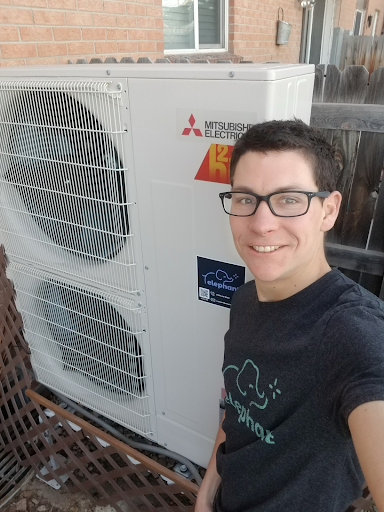 A person standing next to an outdoor heat pump unit installed beside a residential building