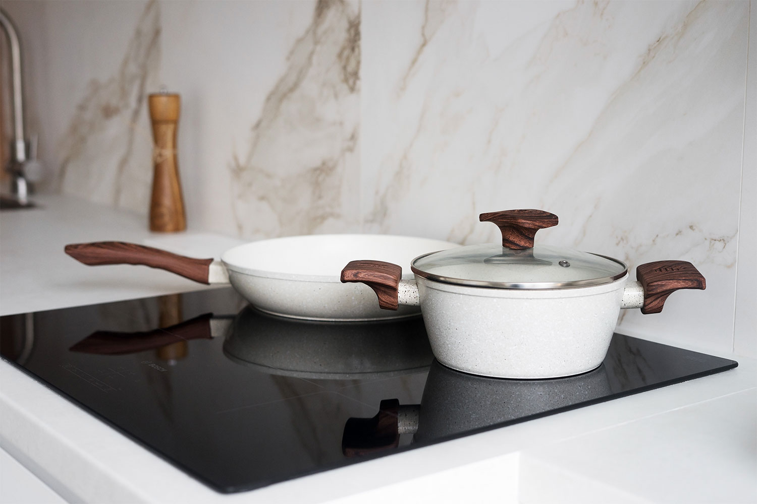 Two light-colored cooking pots with wooden handles sitting on a sleek black induction cooktop in a modern kitchen