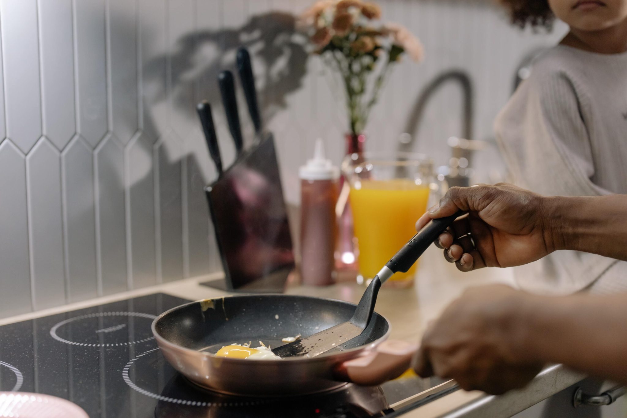 A person cooking an egg in a frying pan on an induction stovetop in a kitchen