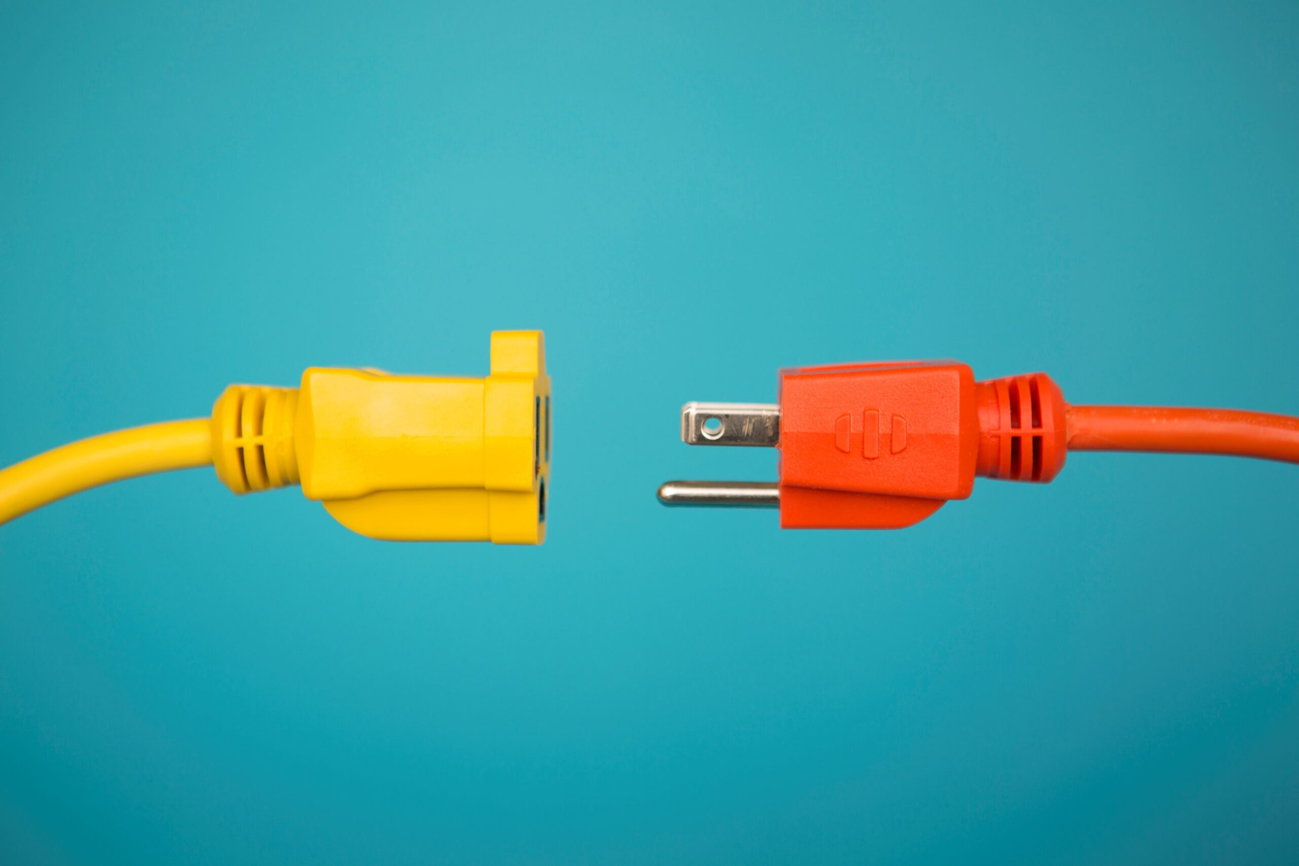 A close-up of a yellow extension cord socket and a red electrical plug positioned just before being connected, against a blue background.