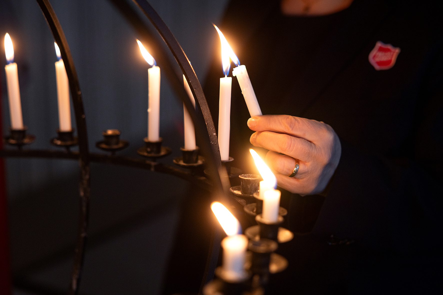 Foto: Nærbilde av deler av en lysglobe, og en hånd som er i ferd med å tenne et lys ved å holde det inntil ett annet lys. En rekke tente lys er plassert bortover i den svarte metallgloben.