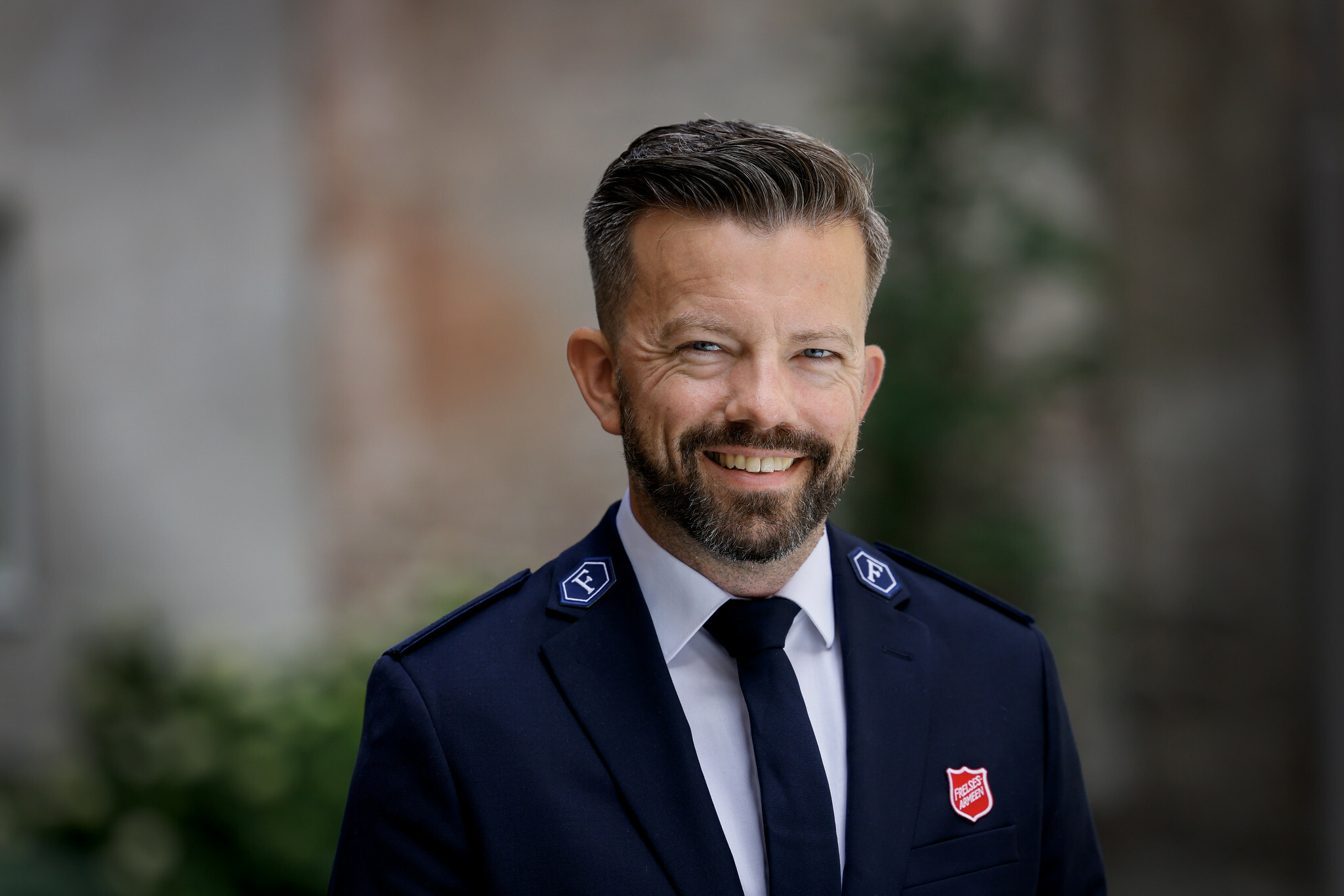Foto: Mann i uniform fra Frelsesarmeen. Han har skjegg, kort hår og smiler.