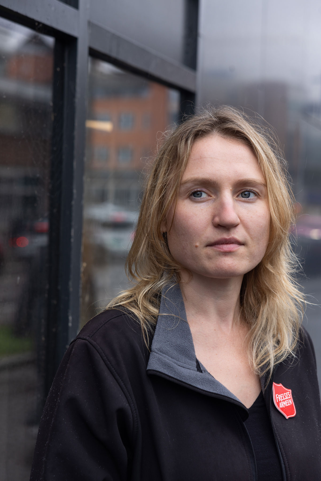 Nærbilde av en kvinne i 30-årene medmørk blondt hår. Hun har et rødt og hvitt frelsesarméskold på høyre siden av den svarte jakken,.