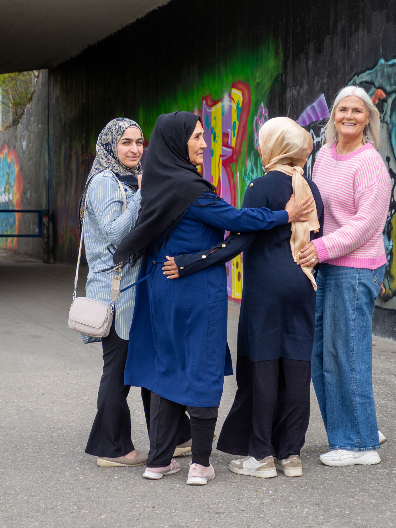 Foto: Fire kvinner, en nordisk med hvitt og tre med hijab står foran en undergang som har tagging på betingveggene.
