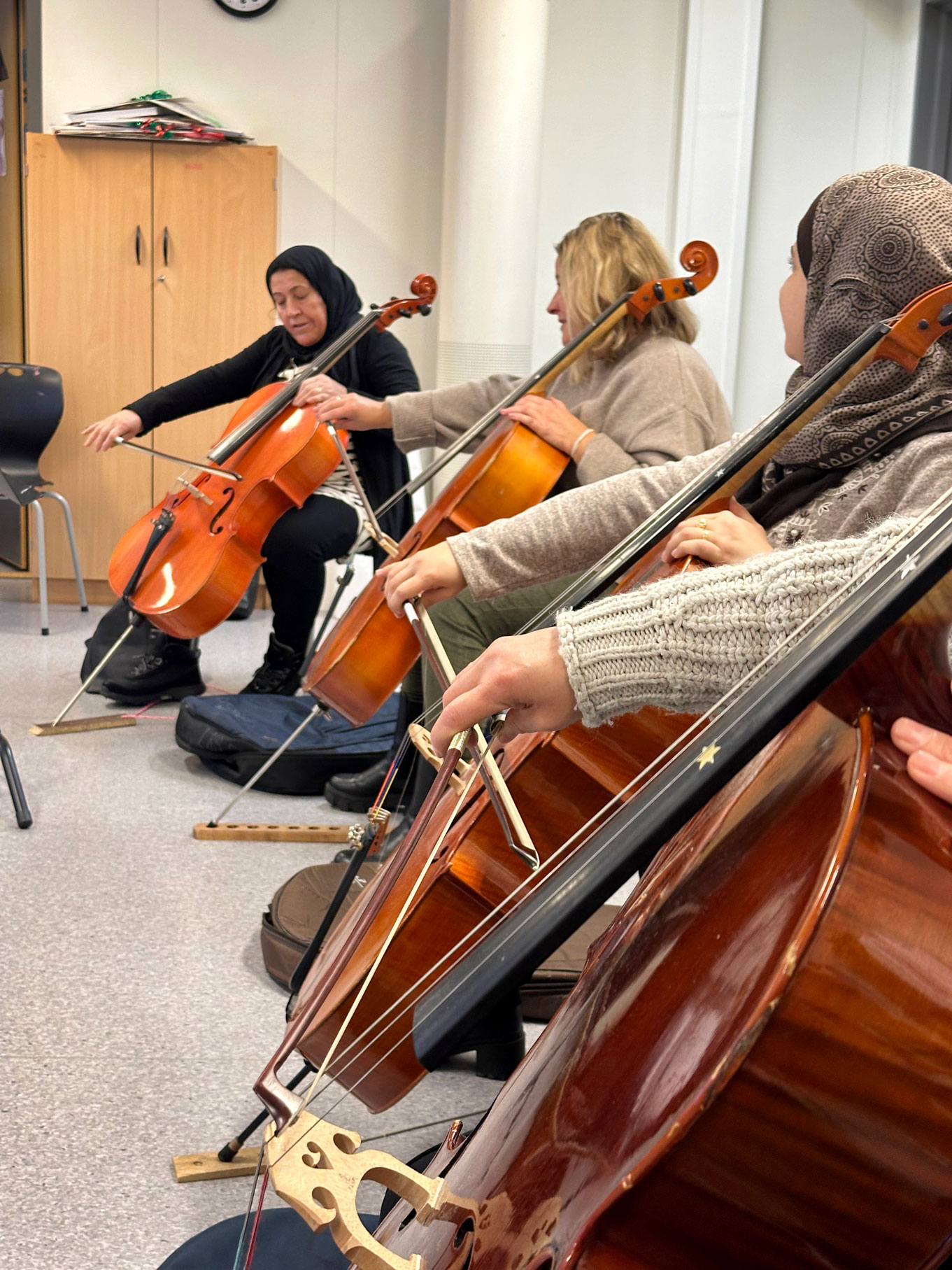 Foto: Fire celloer på rekke og rad. Vi kan se ansiktet til den første som spiller. Hun har på seg en svart hijab. Ved side av henne sitter en blond kvinne i ullgenser og så ser vi nok en hijab og kun ene hånden til den siste, som har på seg en beige ganser.