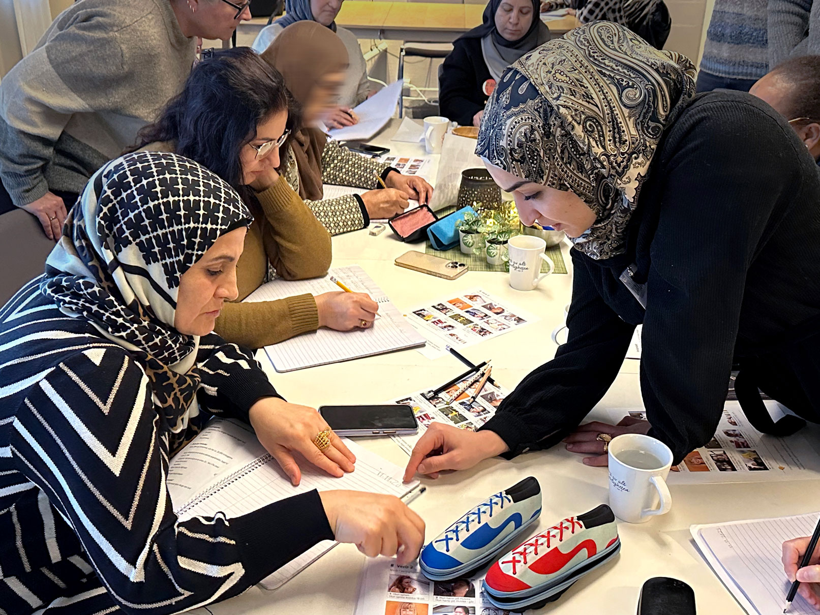 Foto: En kvinne med hijab hjelper en annen med å lese og skrive i en bok.