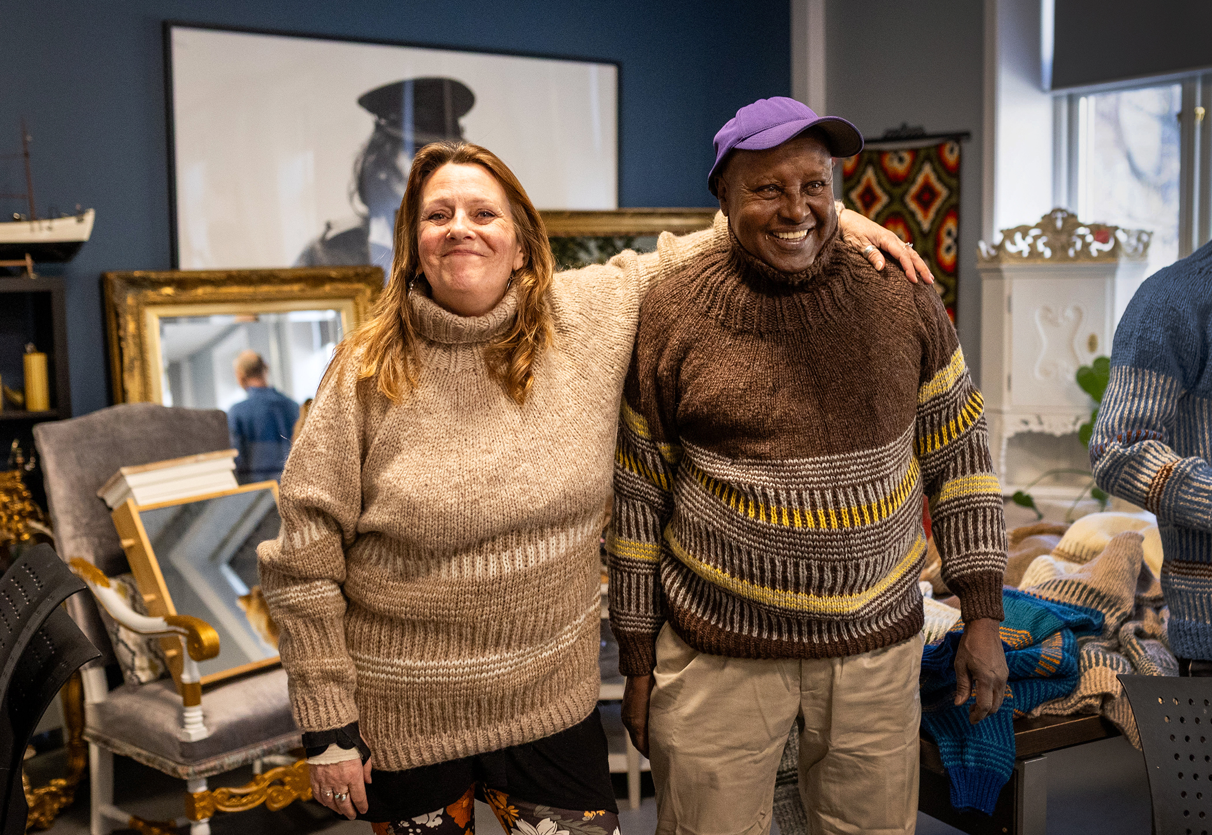 Foto: Hvit kvinne holder armen om en svart mann. De har på seg hver sin tykke ullgenser med samme mønster, men i ulike farger. De står i et rom der flere speil er satt opp, slik at de kan se seg.