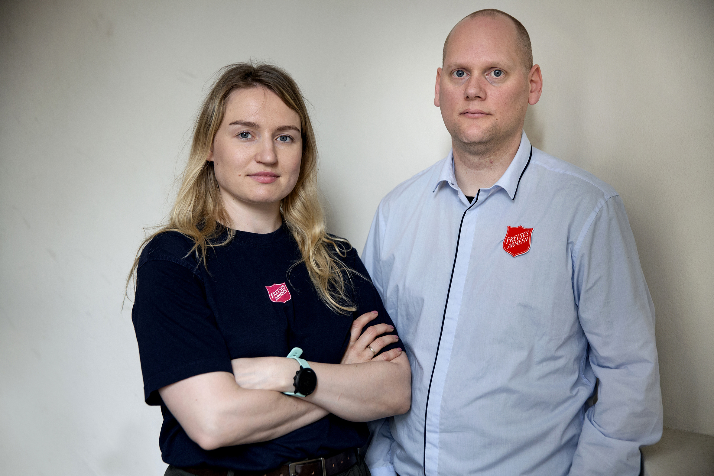 Foto: Kvinne og mann i 30-årene står i henholdsvis mørk T-skjorte og lys skjorte med logoen til Frelsesarmeen på. Hun har langt hår, han er glattbarbert.
