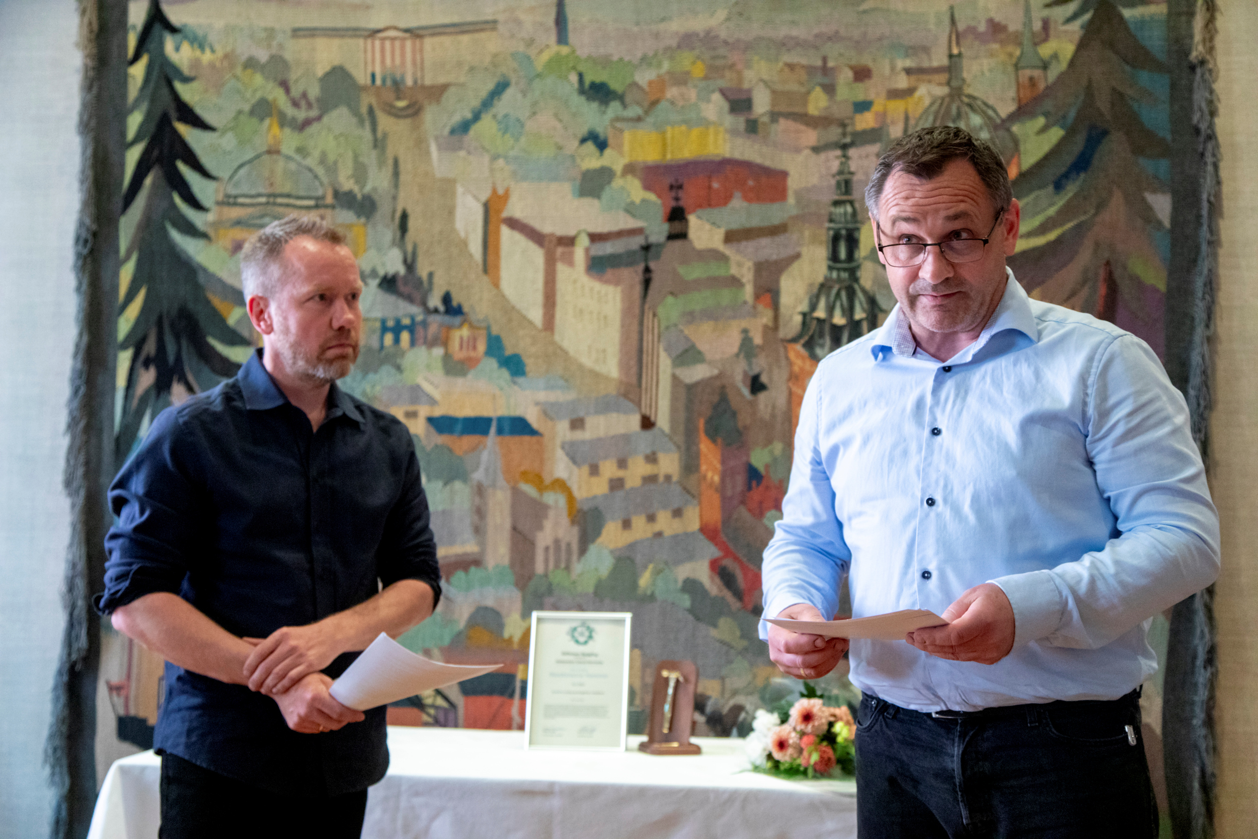 Foto: To menn holder en tale. I bakgrunnen står det et diplom, sleve prisen Stockmanna hammer og en bukett med blomster.