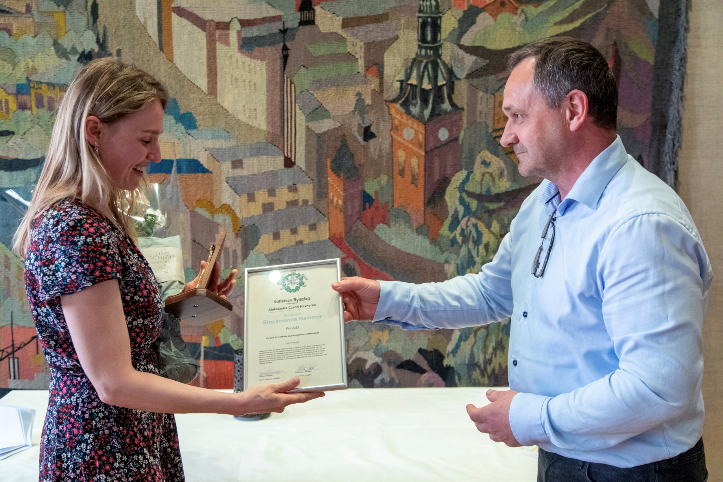 Foto: Mann i blå skjorte deler ut pris til kvinne i blomstrete kjole.