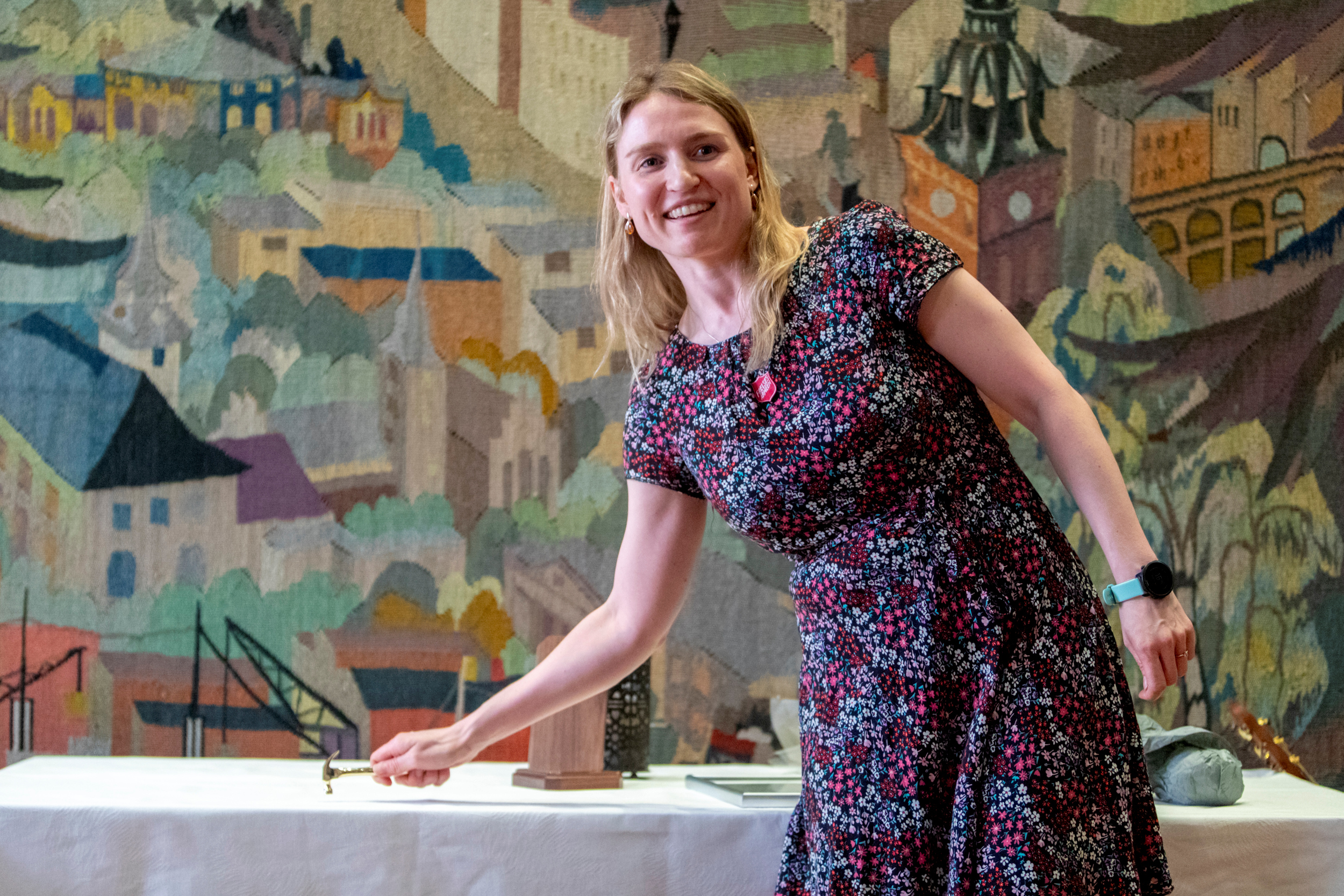 Foto: Av kvinne i kjole som bruker den bittelille hammeren hun har fått tildelt til å slå på den hvite duken på bordet ved henne.