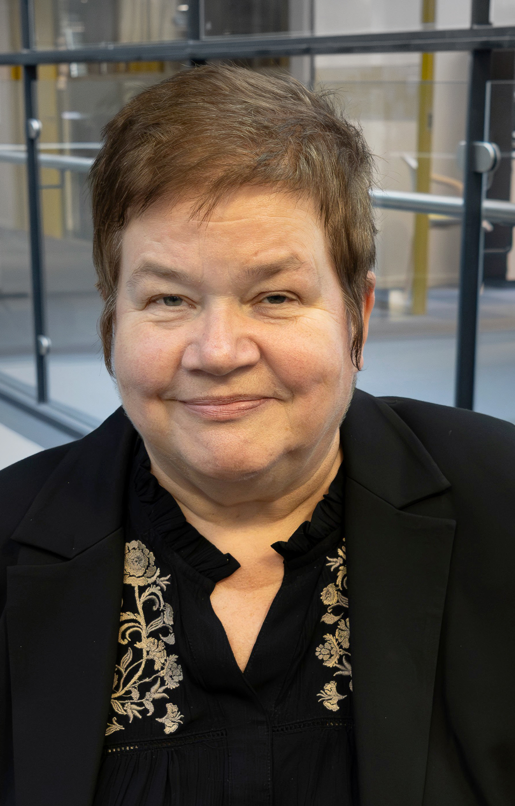 Foto: Kvinne i 50-årene med kort brunt hår tatt i et kontorlandskap.