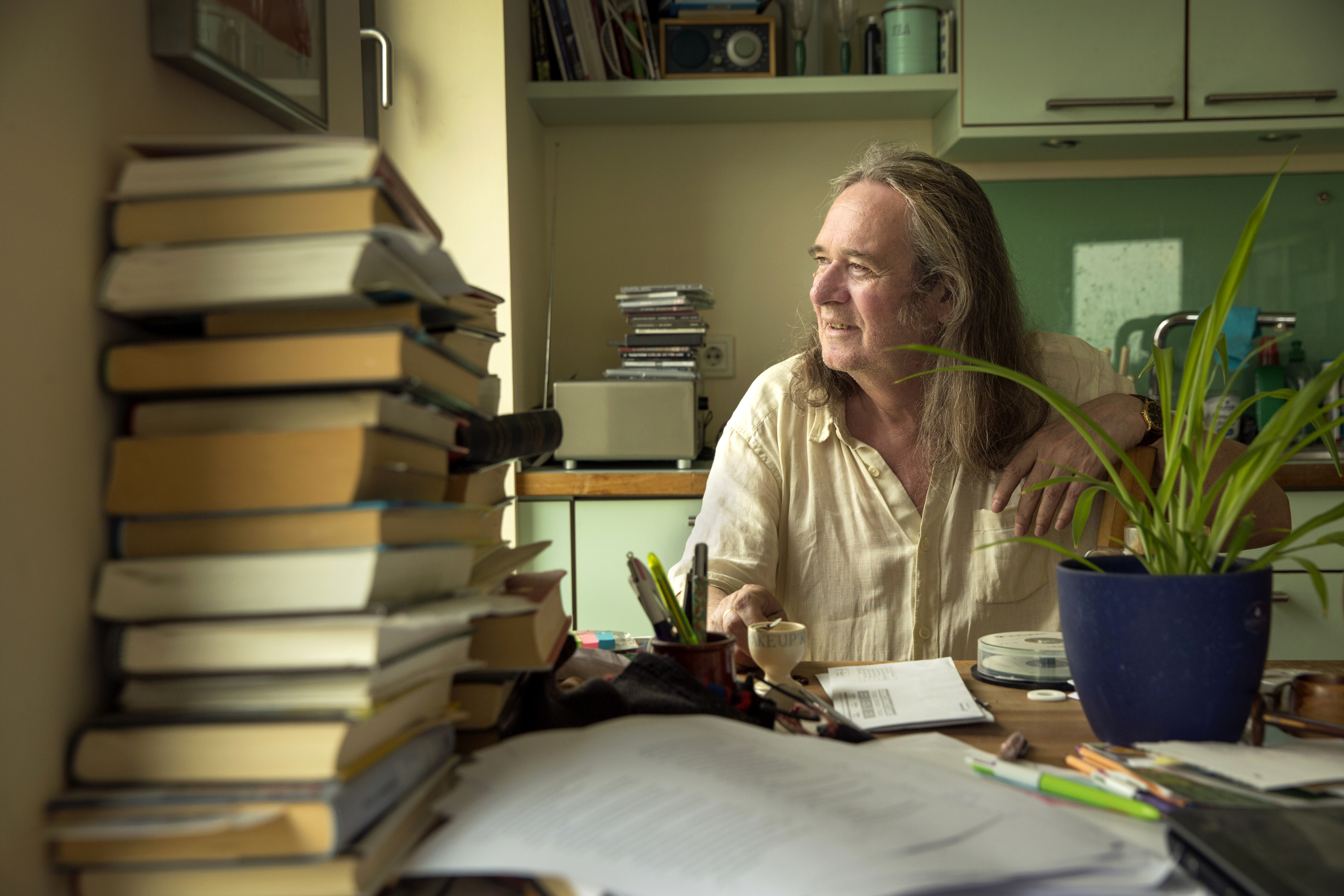 Ingvar Ambjørnsen ser ut av vinduet bak en bokstabel.