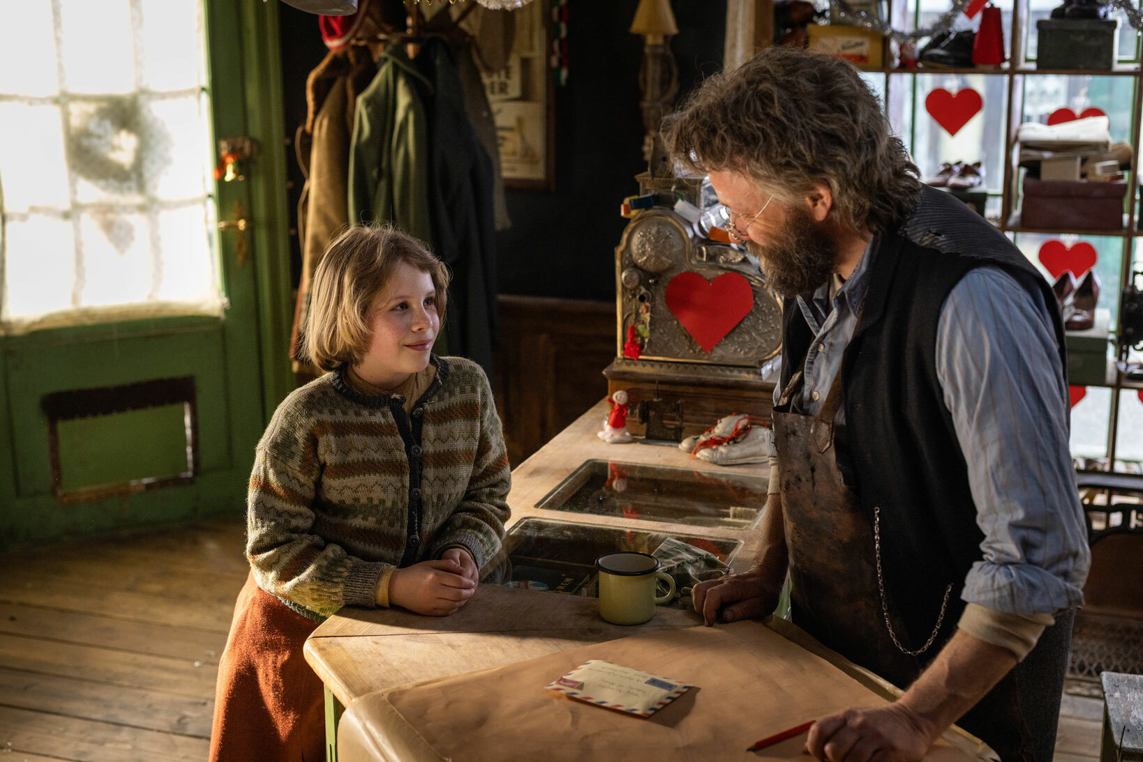 Mann står bak disk med et brev- Snakker med liten jente. Begge i klær fra 40-tallet.