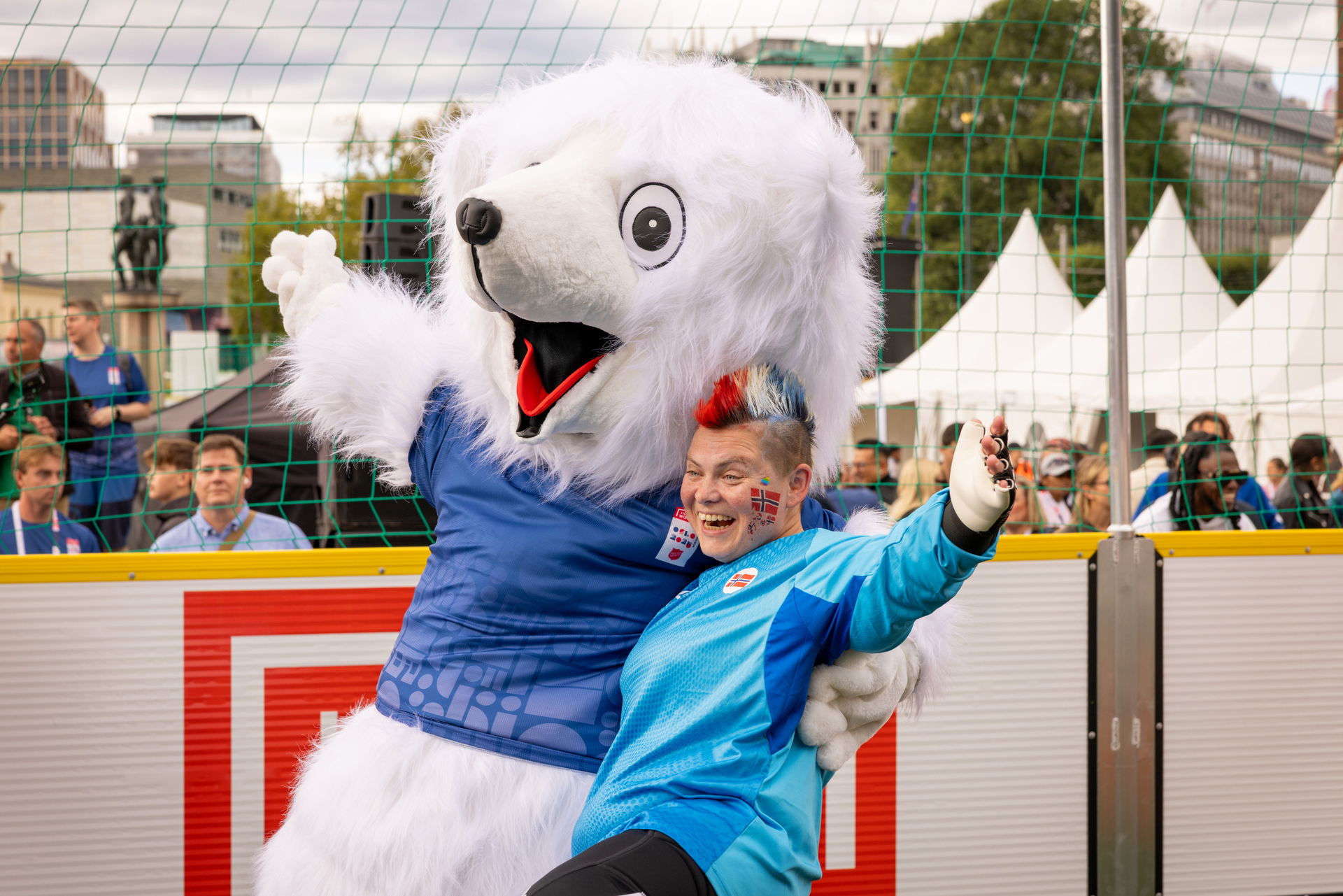 Foto: Fotballspiller i blå trøye og de norske fargene i hanekammen på hodet poserer sammen med en hvit isbjørn-maskot.