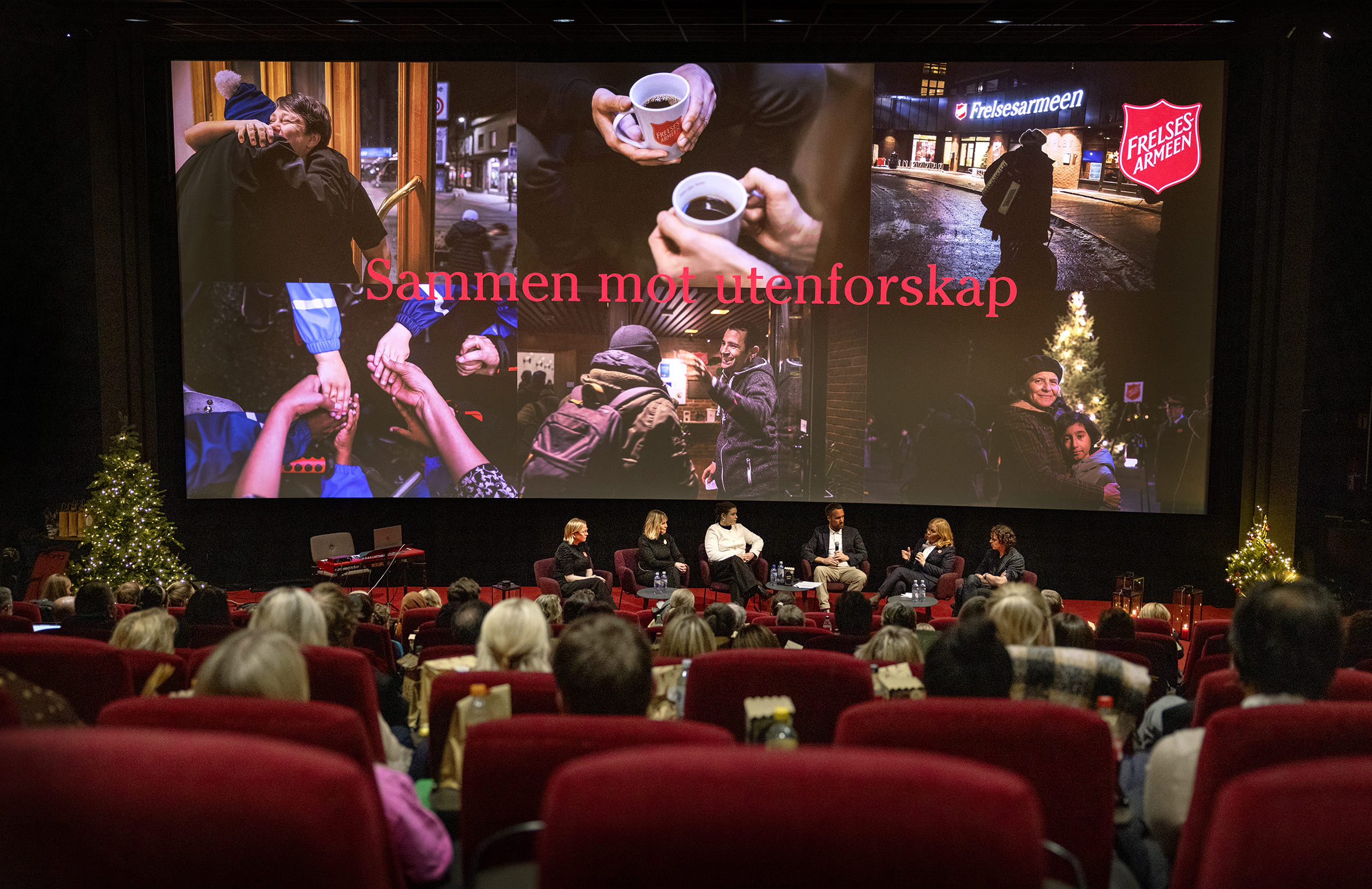 Ser kinosalen ovenifra. Paneldebatt foran. På lerretet står det: Sammen mot utenforskap.