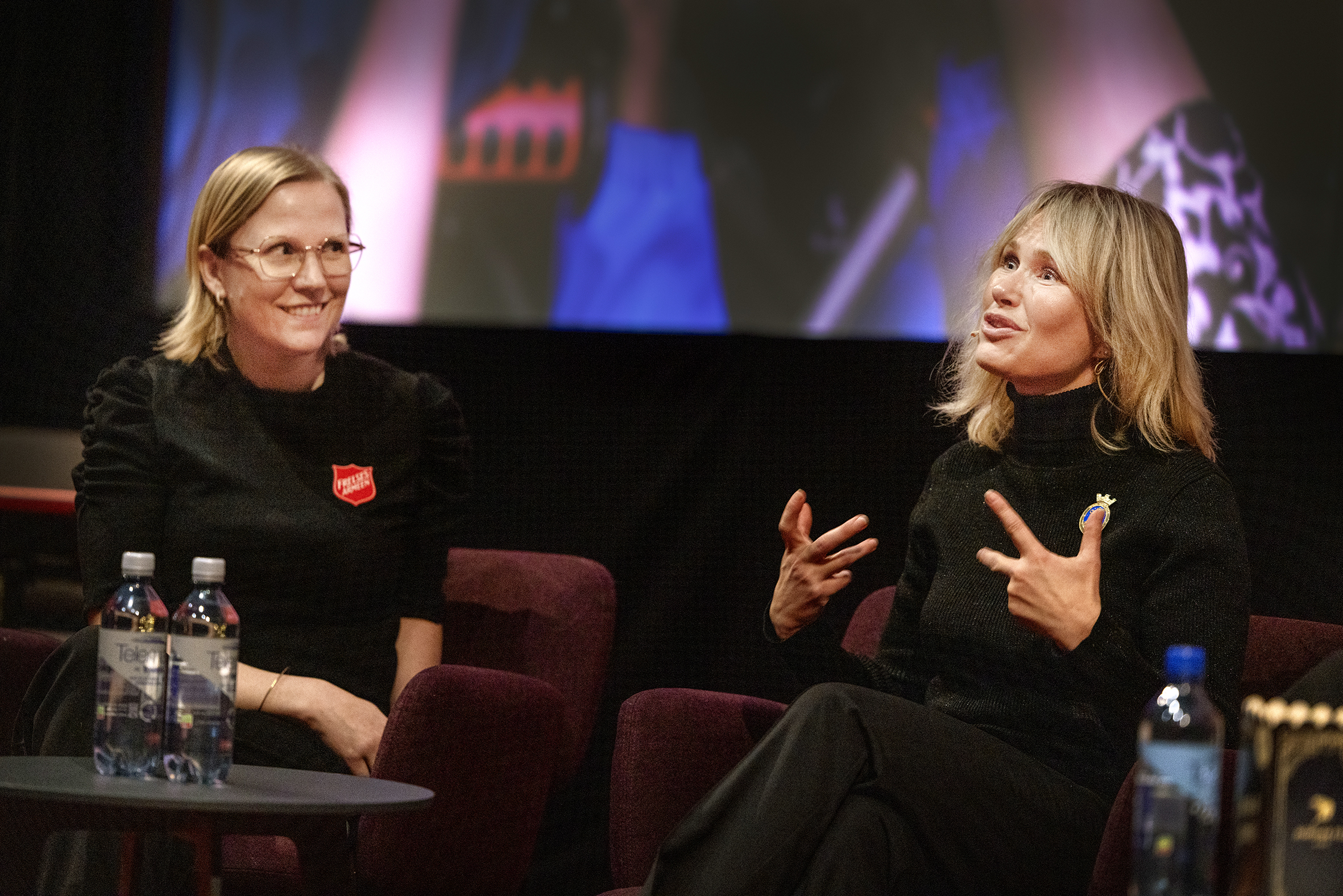 To kvinner sitter og diskuterer i en kinosal foran det store lerretet.