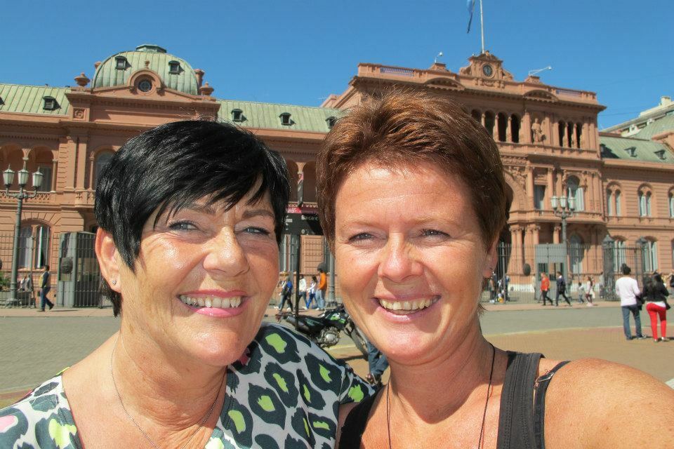 Foto: To kvinner med kort svart og kort rødt hår i en solfylt by.