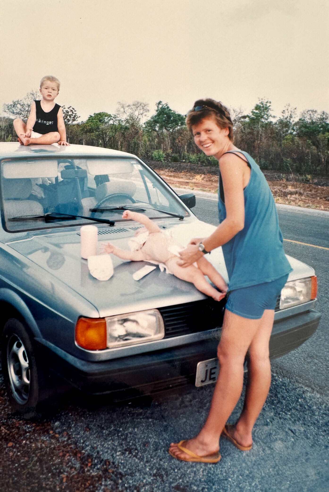 Foto: Ung mor skifter bleie på en unge på panseret. Den litt eldre ungen sitter på taket av bilen.