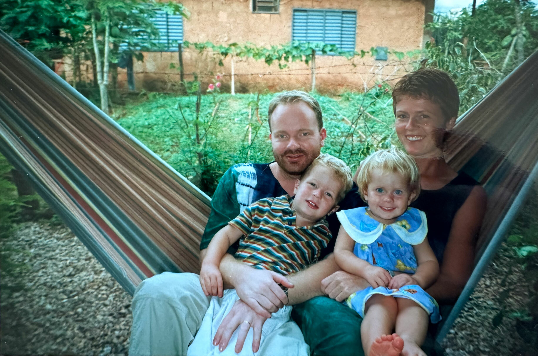 Foto: Ungt par med sønn og datter sitter sammen i en hengekøye. I bakgrunnen er det grønt og landlig.