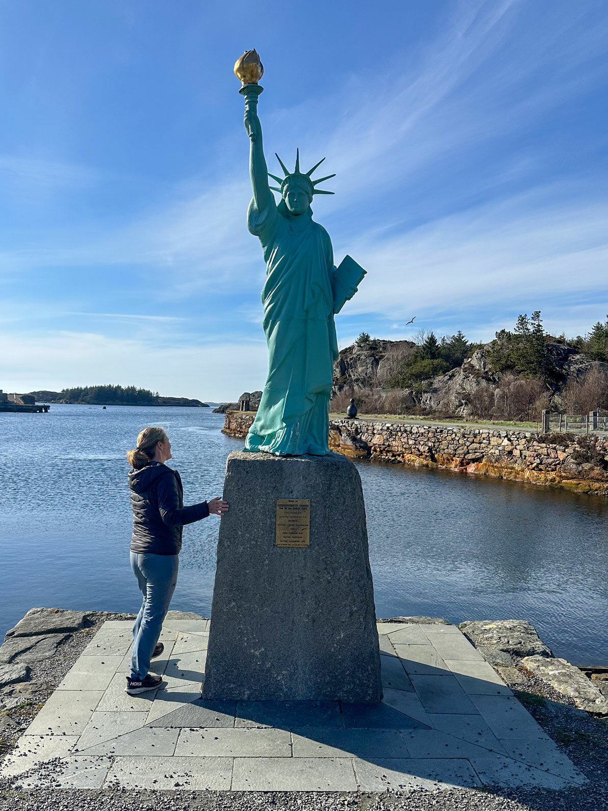 Foto: Kvinne i blå boblejakke står og ser opp på en kopi av Frihetsgudinnen.