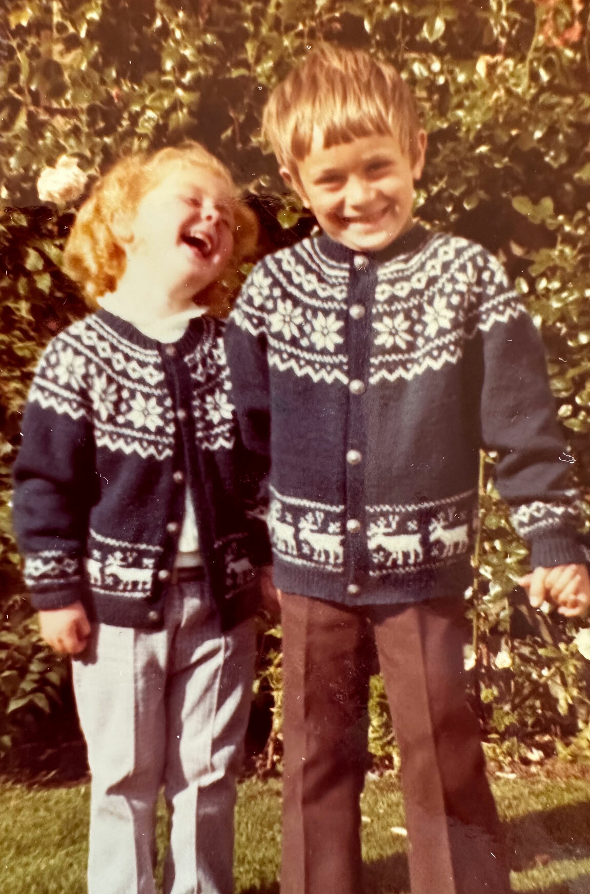 Foto: Liten jente og litt større gutt i like hjemmestrikkede kofter med reinsdyr på.