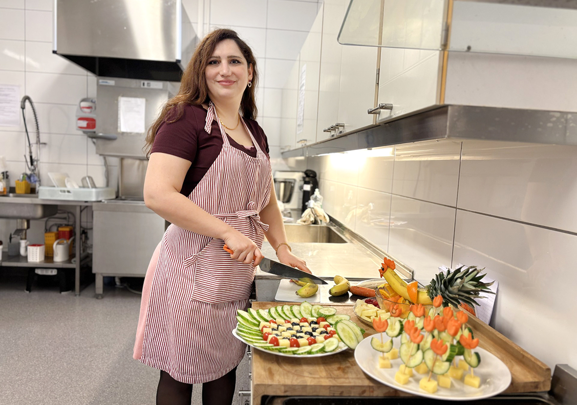 Kvinne med mørkt, krøllete hår i slutten av 30-årene står bak fat med kunstferdig skåret fingermat i friske farger.