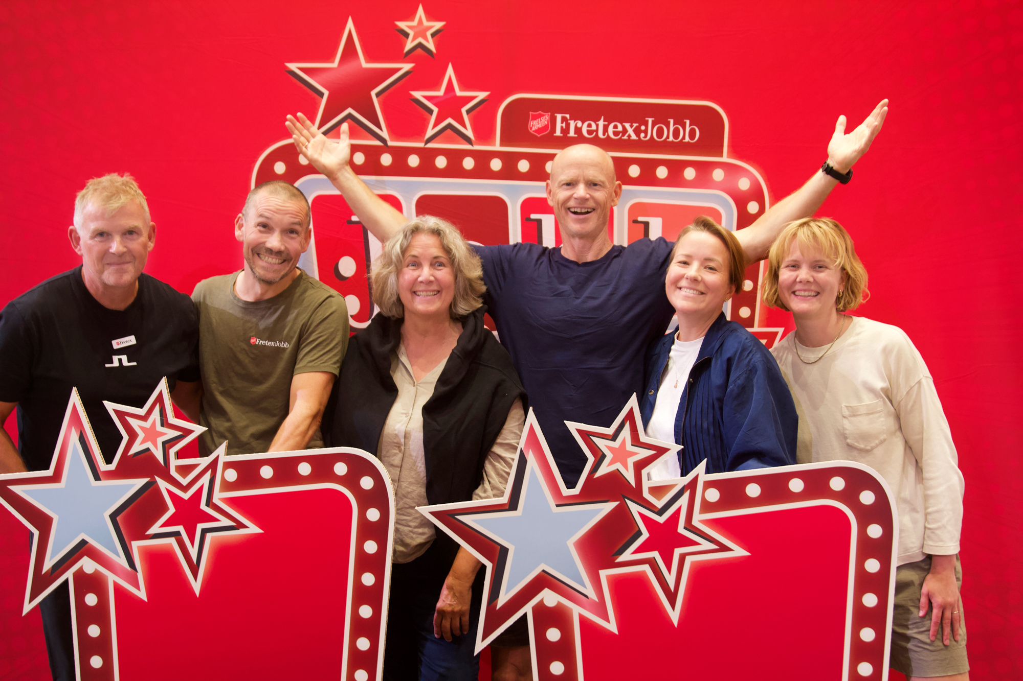 Foto: Tre menn og tre kvinner står foran en rød vegg med stjerner og følelsen av gameshow. Alle smiler bredt, og en mann slår ut hendene.