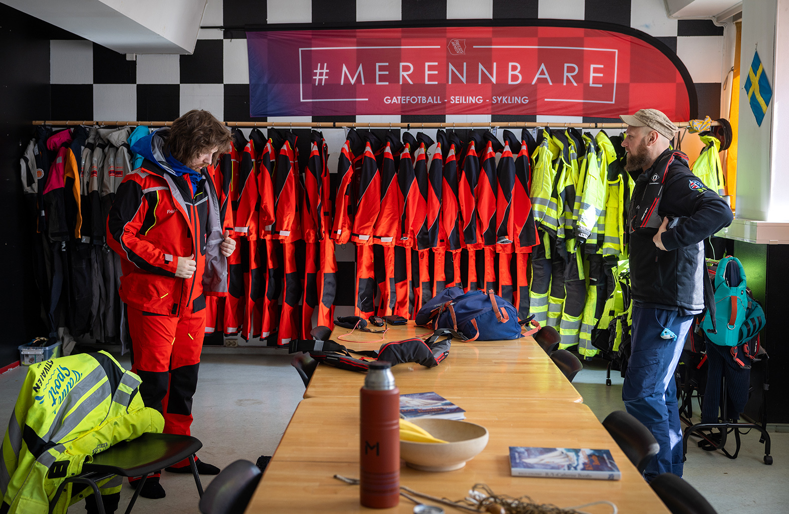 Foto: To menn som kler på seg seilerutstyr. De står mot hverandre.