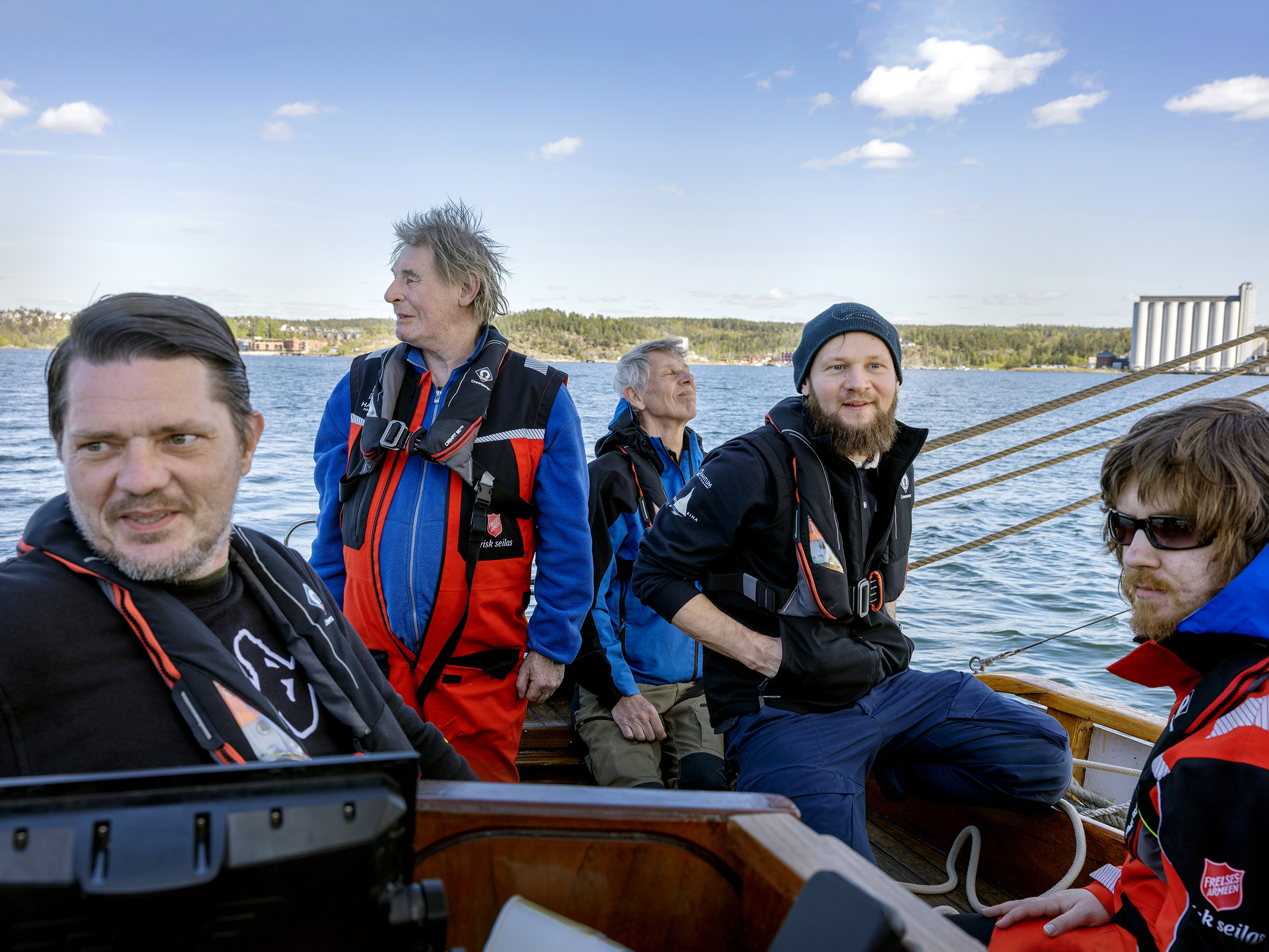 Foto: Fem lykkelige og smilende seilere sitter bak i båten.
