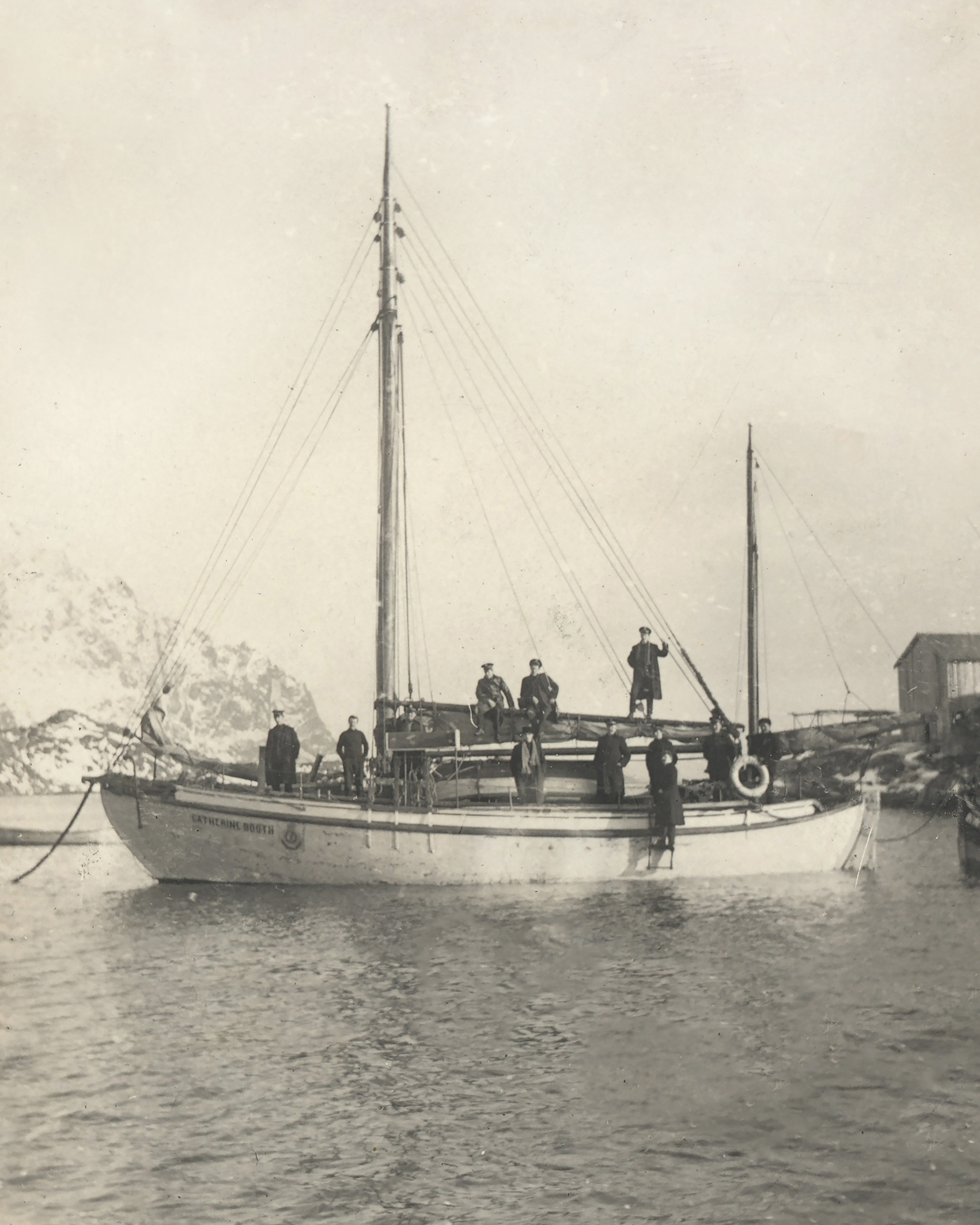 Foto: Gammelt svart-hvitt-bilde av en skute i vannet uten seilene oppe. Rundt på båten står 6-7 menn.