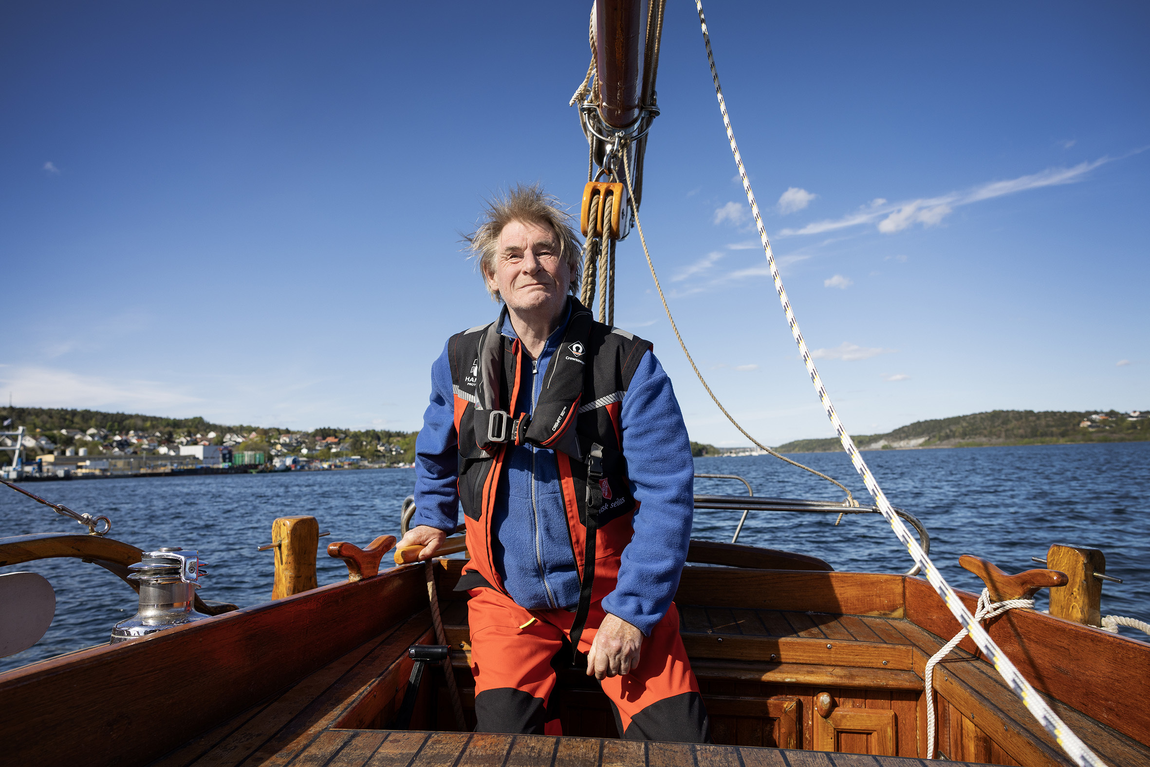 Foto: Mann i 60-årene sitter og holder i roret på seilbåten.