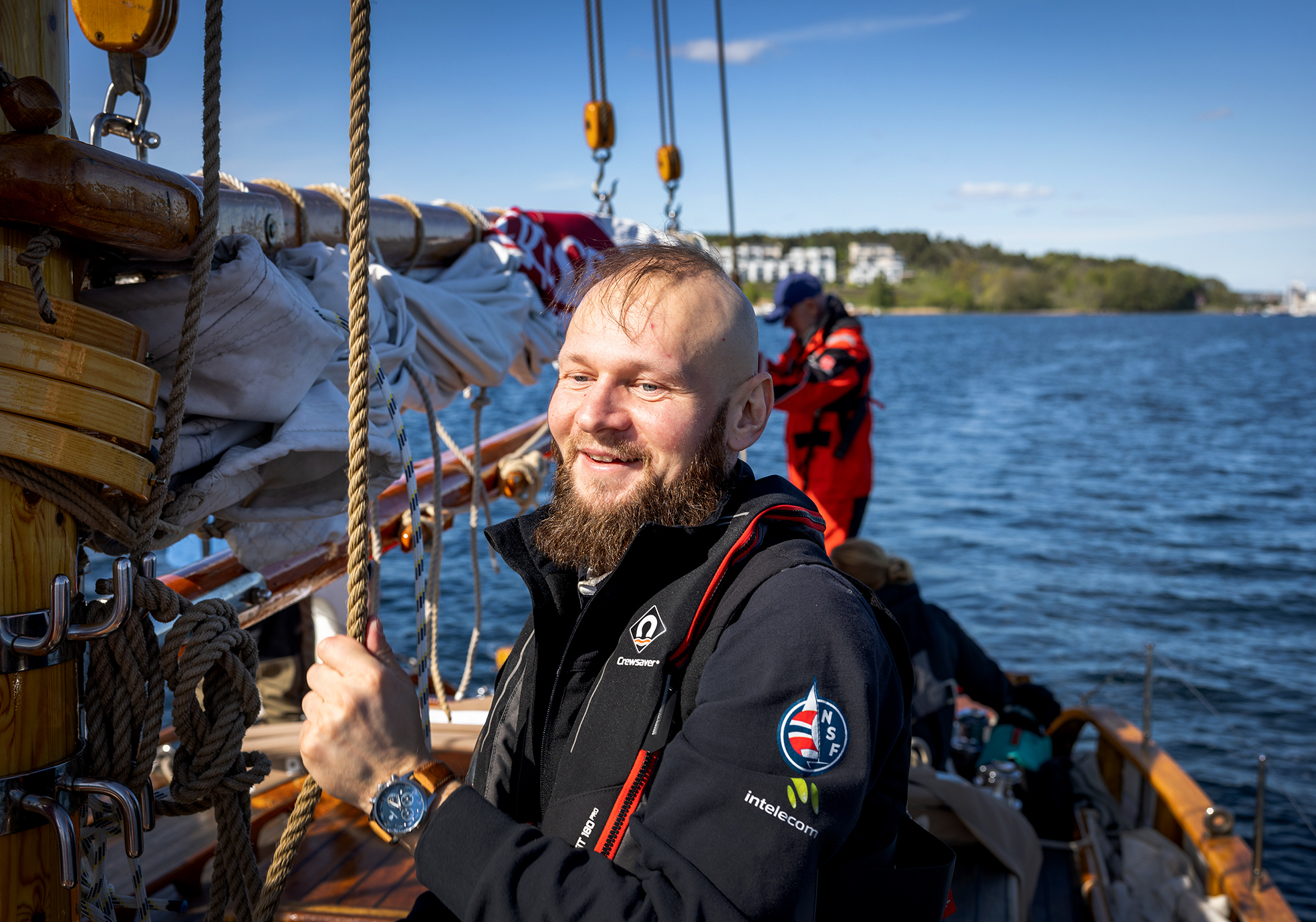 Foto: Mann i blå seilerklær med redningsvest. Han er nesten skallet, men har