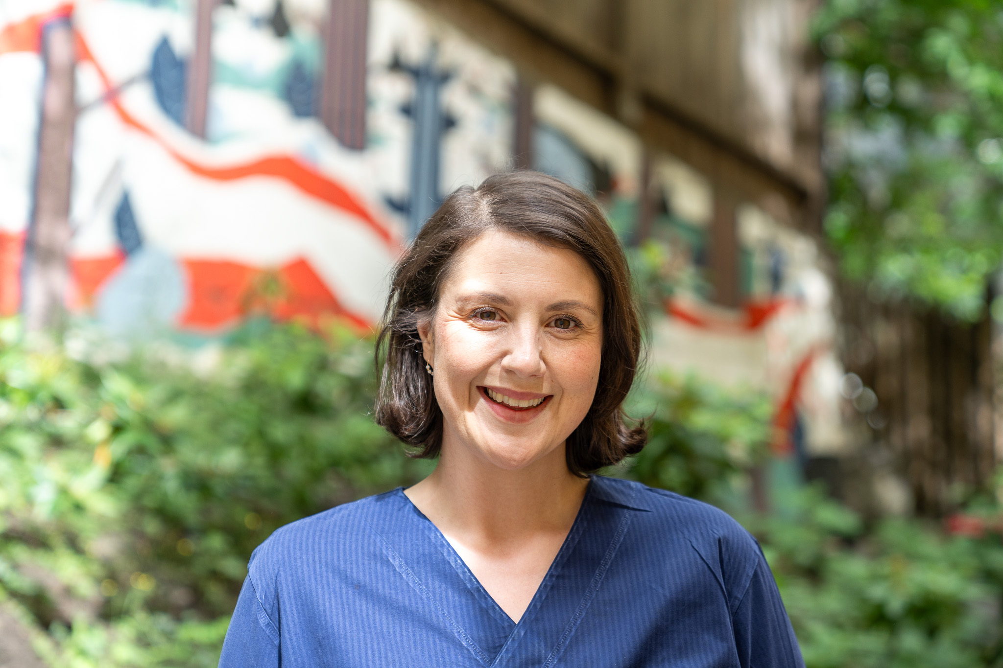 Foto: Av smilende kvinne med mørkt hår i blå helseuniform.