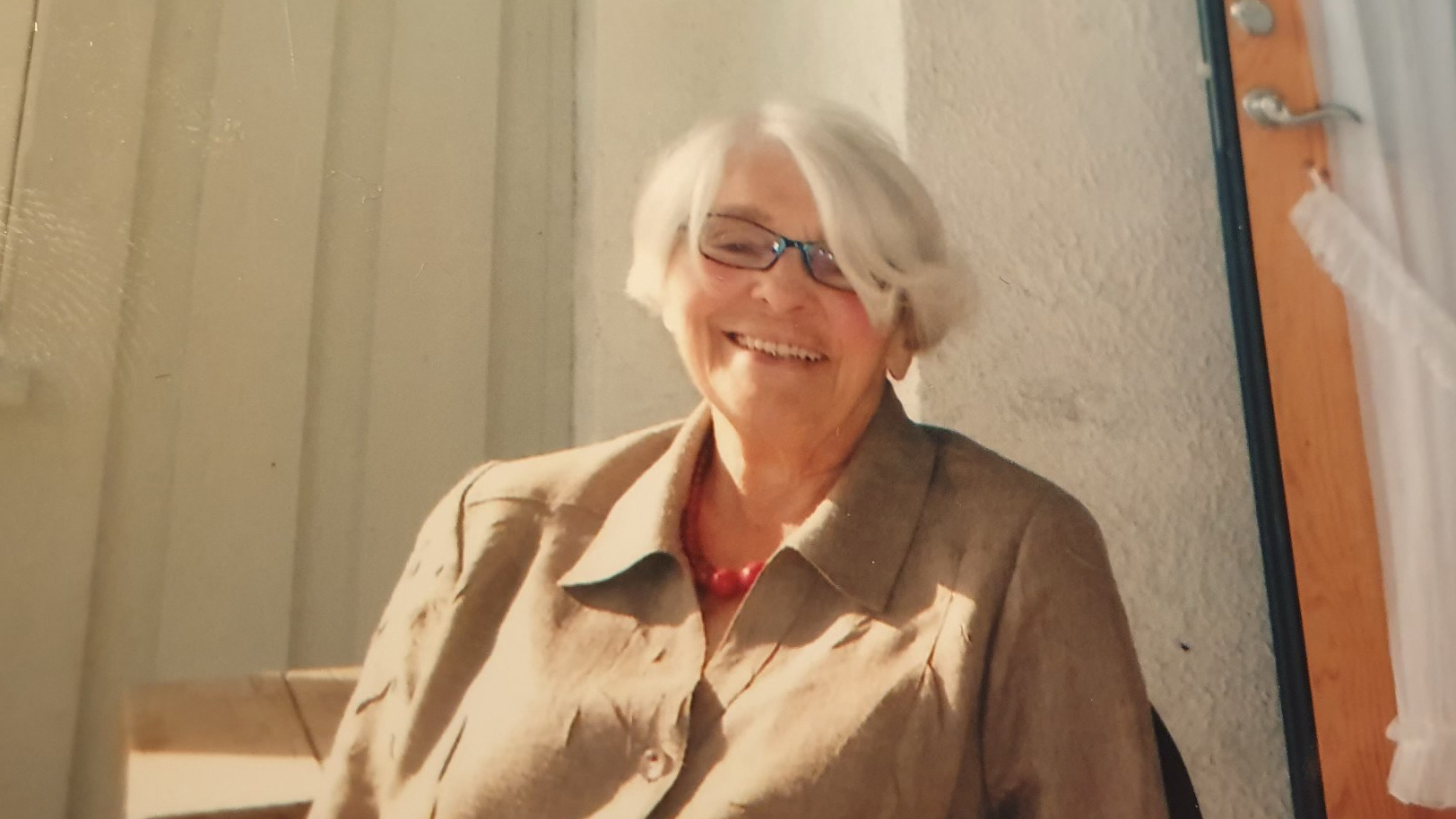 Foto: Gråhåret, smilende kvinne med briller. Bildet er litt utydelig.