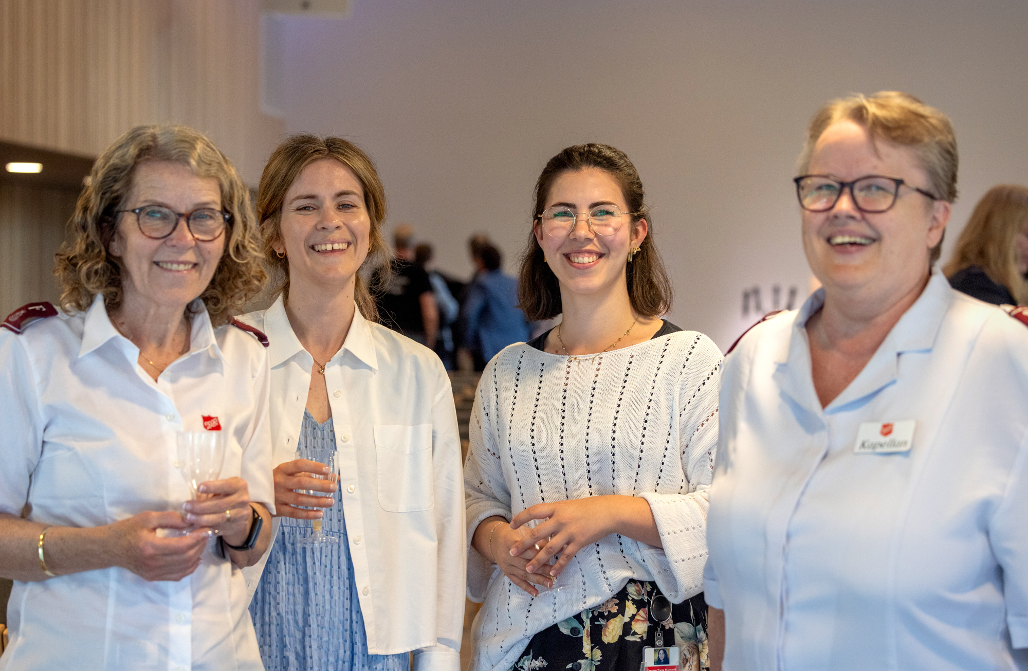 Foto: Fire kvinner i lyse klær står på en rekke bortover. Alle smiler.