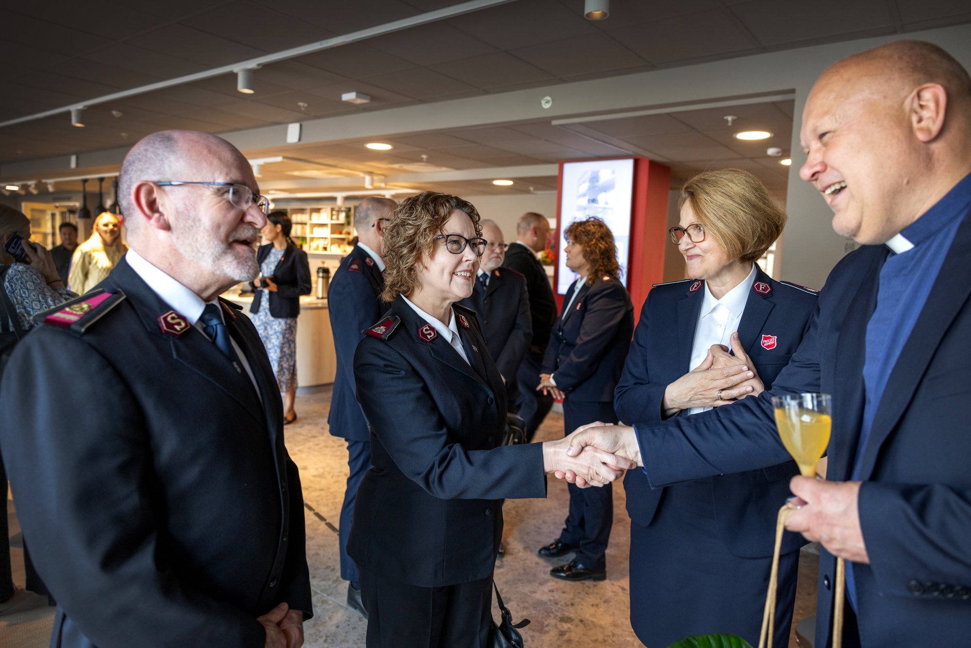 Foto: Mann med blå prestesnipp står ved tre personer i uniform fra Frelsesarmen. Han hilser på den ene kvinnen.
