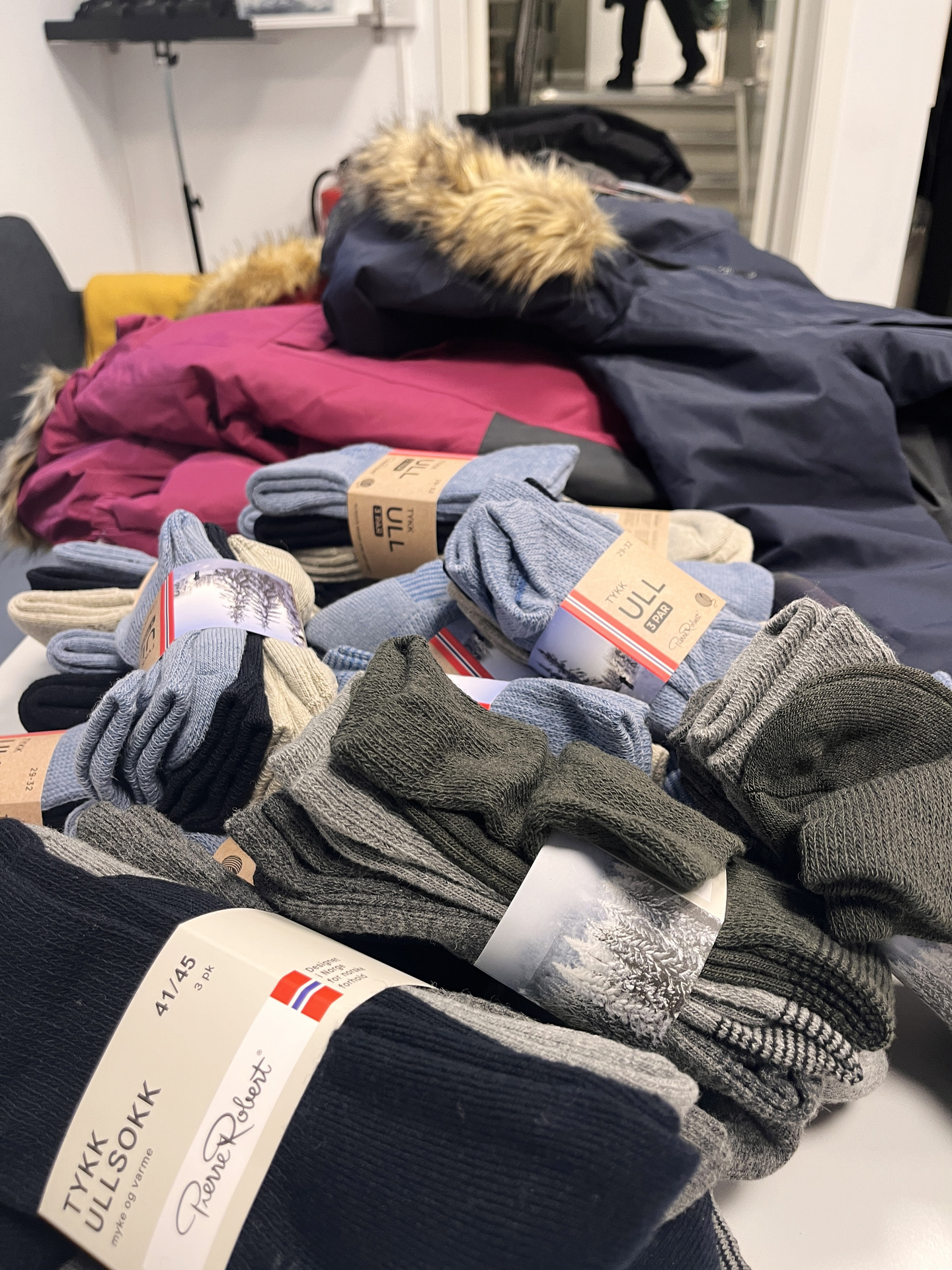 Ulltøy og varme klær ligger klart på et bord til henting av foreldre som trenger hjelp for å ha råd til vamt tøy til barna sine.