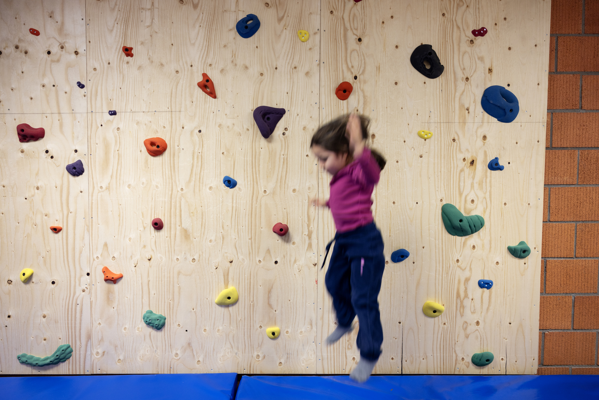 Foto: To bilder etter hverandre der det første viser en liten jente som hopper ned fra en klatrevegg med fargerike grep å holde i. Den andre viser samme jente som står ved en rød lekekomfyr.