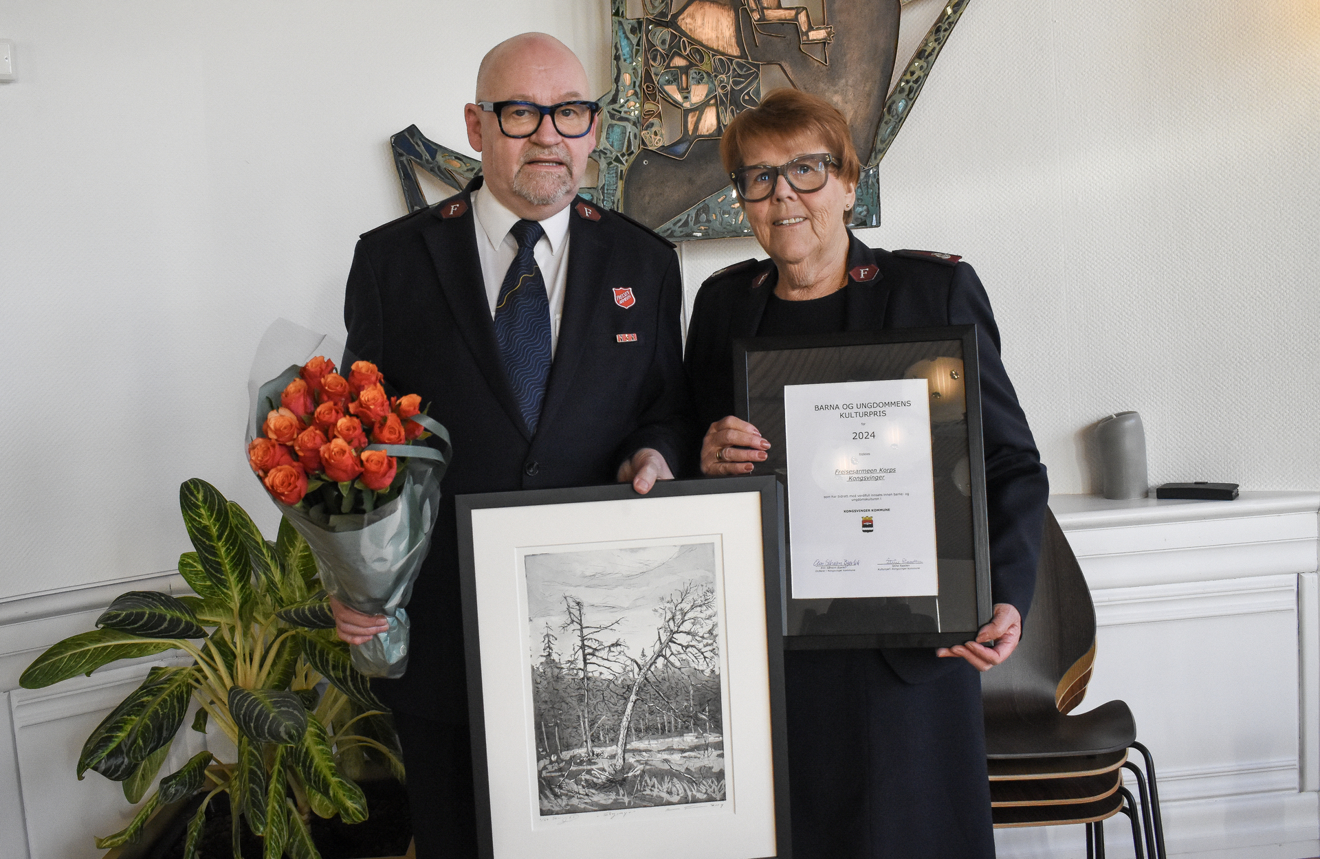 Foto: Mann og kvinne i 60-årene holder opp et diplom, et kunstverk og en bukett med rødoransje roser. Begge har på seg uniform fra Frelsesarmeen.