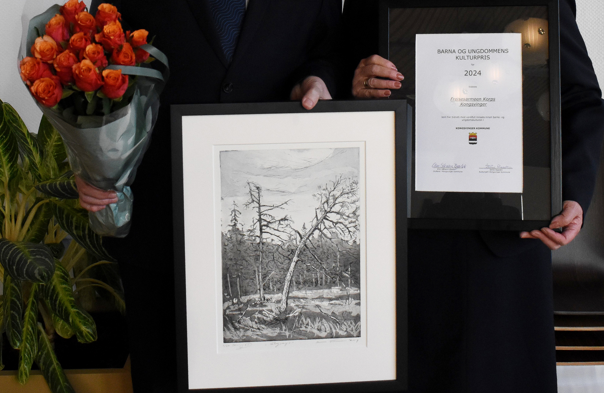 Foto: Nærbilde av blomster, kunstverk med trær og diplom der det står "Barna og ungdommens kulturpris for 2024 tildeles Frelsesarmeen korps Kongsvinger".