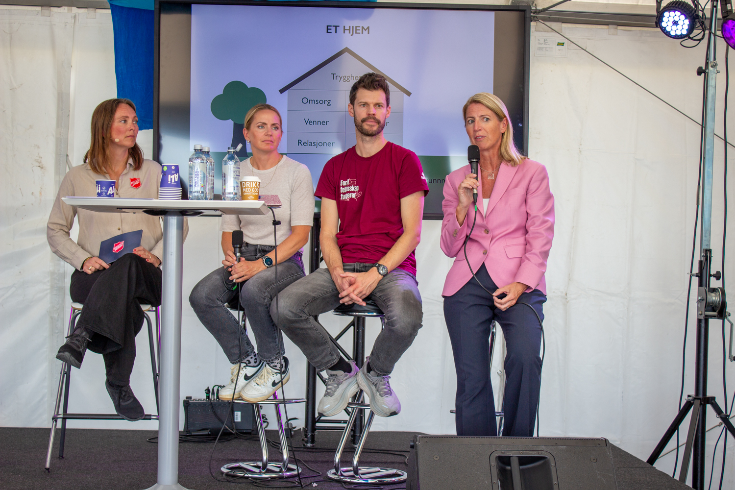 Foto: Fire personer på rekke, tre kvinner og én mann, sitter i et panel i det samme teltet med skjerm bak seg med tegning av en bolig.