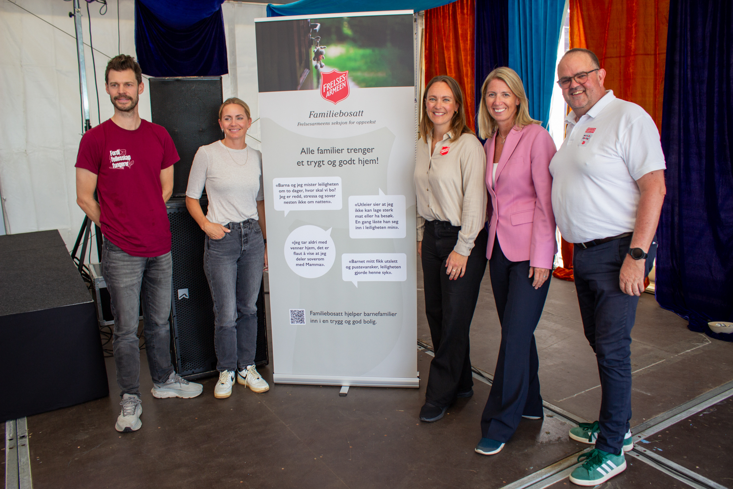 Foto: To menn og tre kvinner står foran en roll-up inne i teltet. Den har logoen til Frelsesarmeen på og har snakkebobler med sitater fra barn.