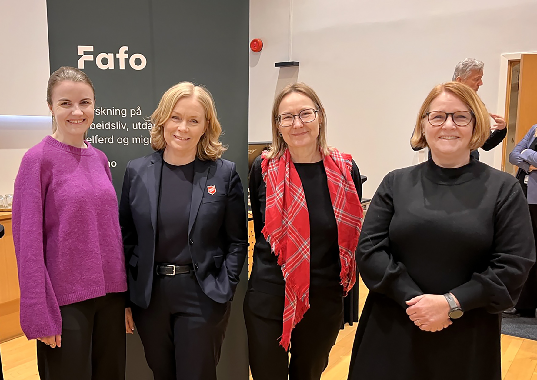 Foto: Fire damer på rekke foran en roll-up der det står Fafo.