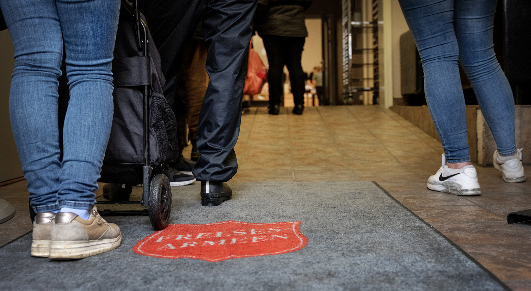 Foto: Mennsker står i kø. Teppet på gulvet er fra Frelsesarmeen.