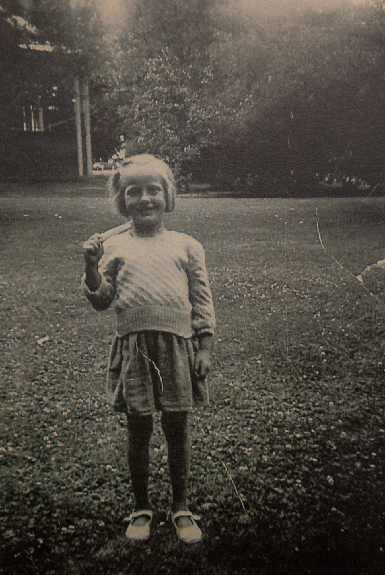 Foto: Gammelt svart-hvitt-bilde av en liten jente med kort, lyst hår som står på en plen.