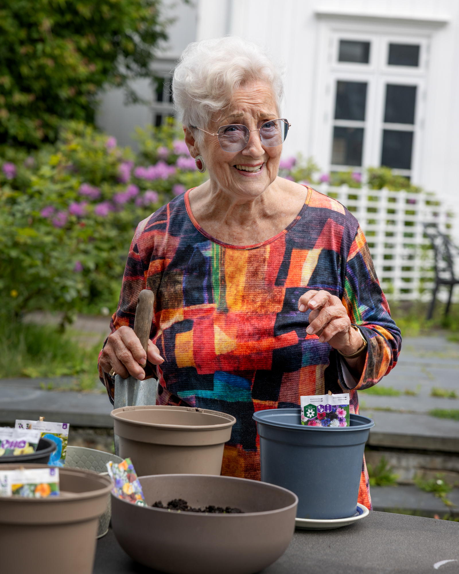 Foto: Eldre kvinne i 80-årene som står ved noen potter der hun har sådd planter.
