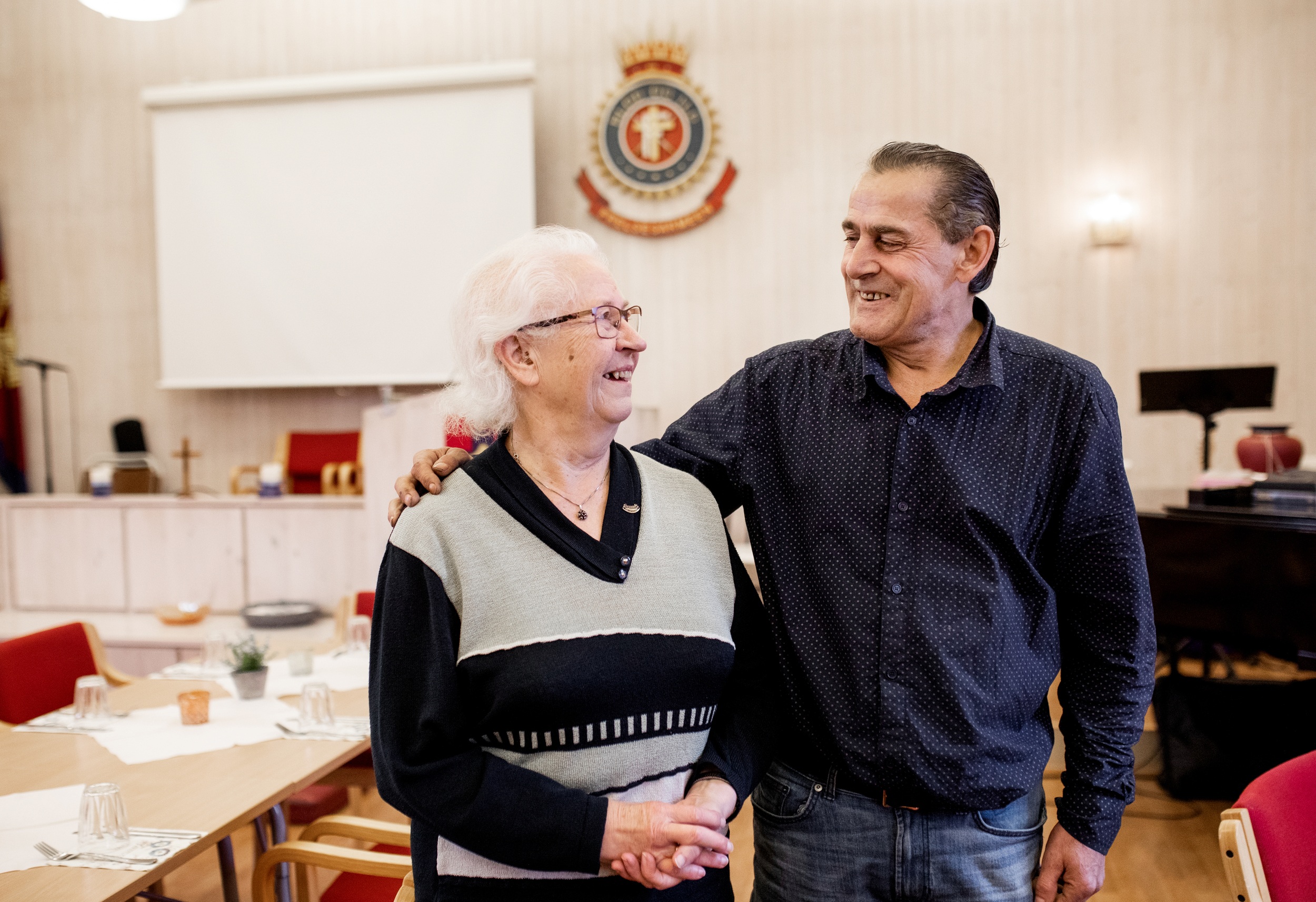 En mann i femtiåra holder armen rundt en eldre kvinne. De smiler og ser på hverandre.