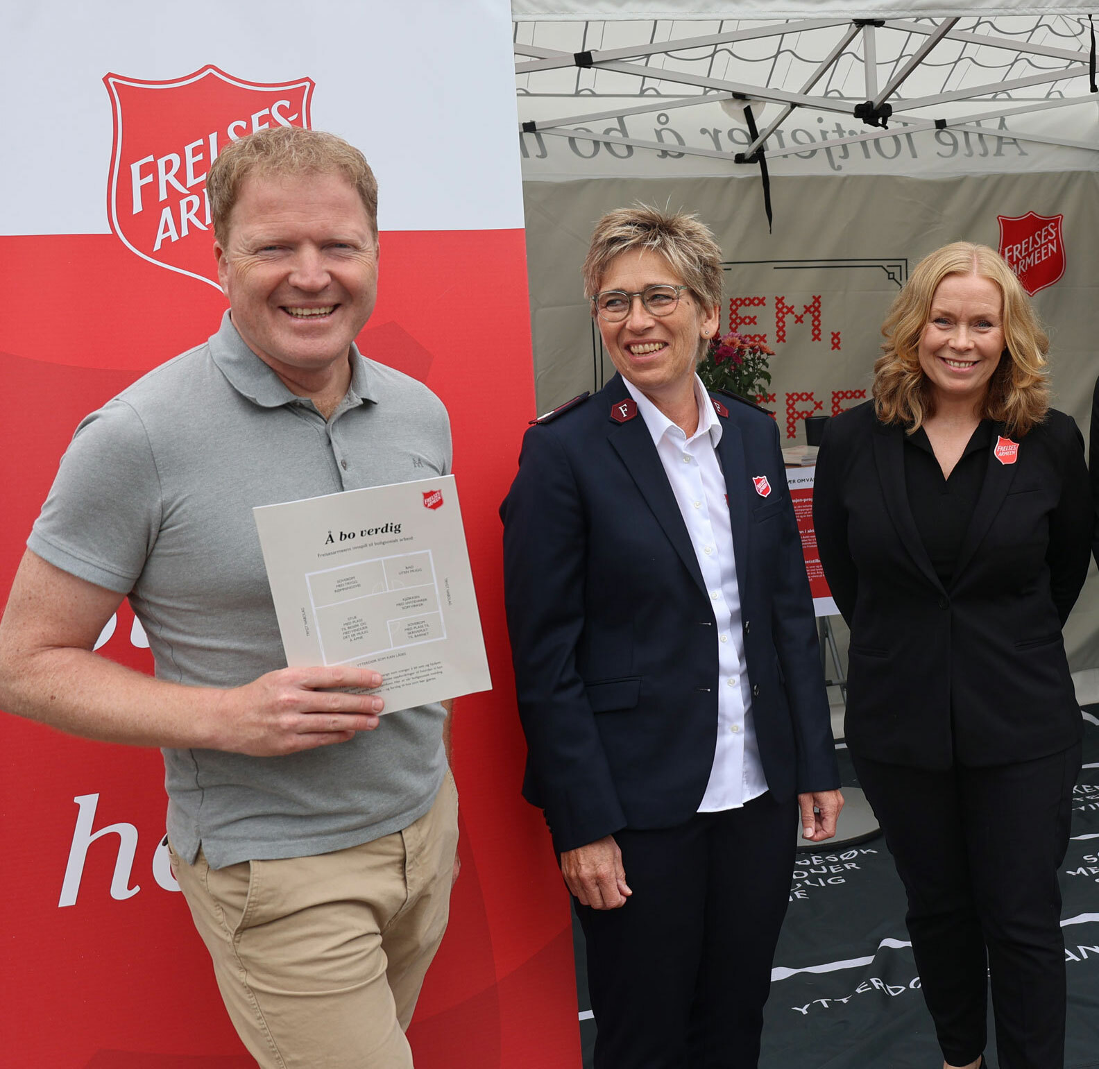 Mann holder fram en rapport. Både han og to kvinner ved siden ac smiler.